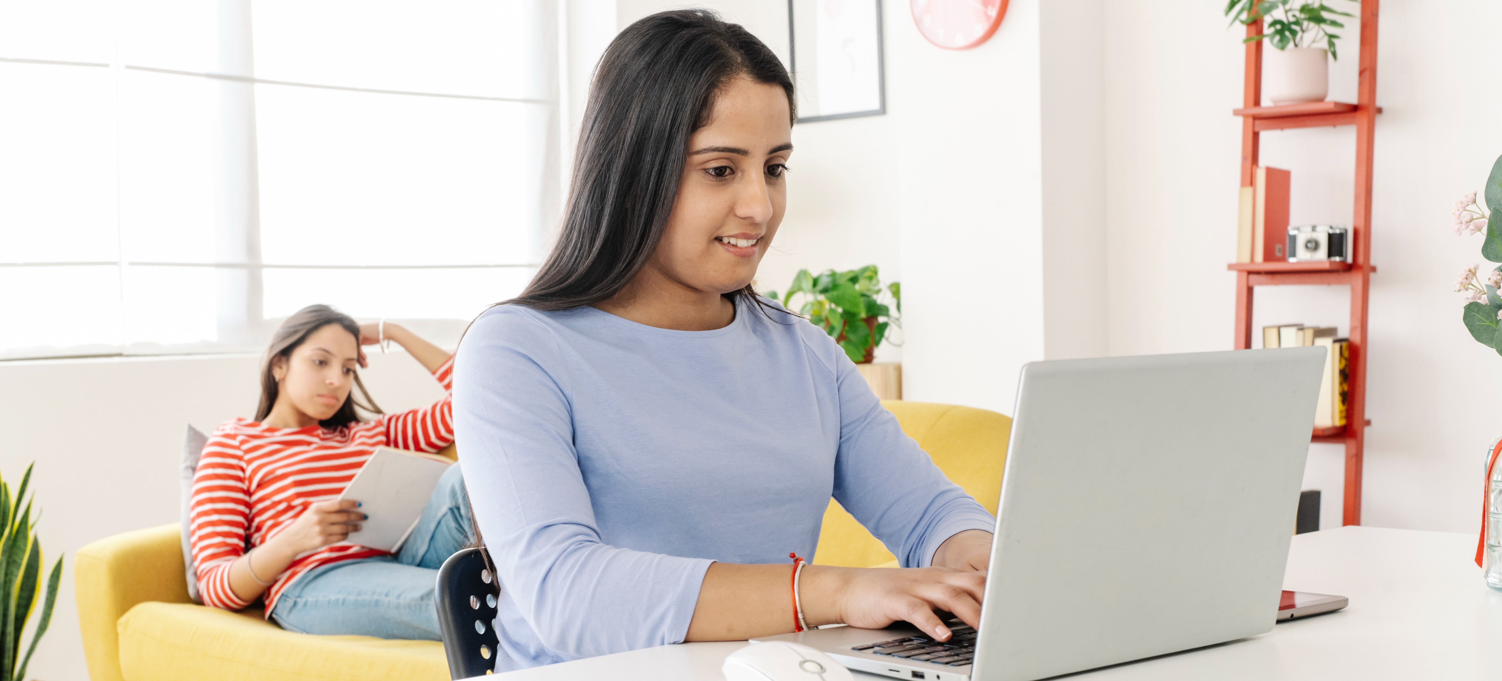 [Featured Image] A young professional in their living room at home researches on their laptop to determine if they wants to earn a BTech or BSC. 
