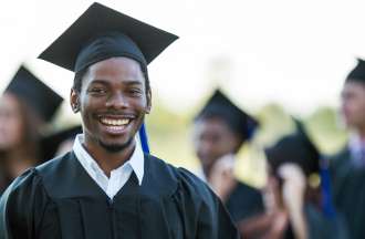 [Featured Image]:  A man wearing a black cap and gown smiles as he graduates as a social science major.