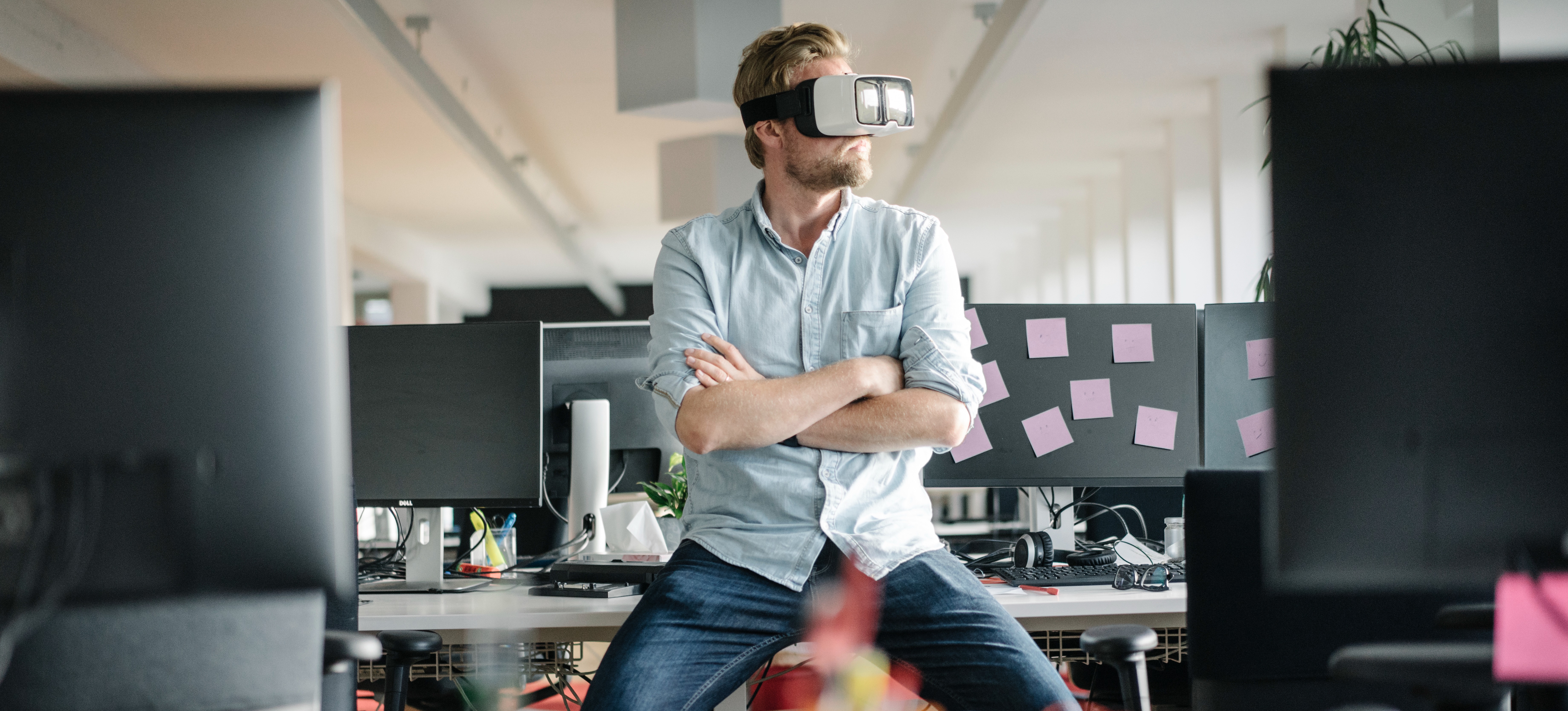 [Featured Image] A creator in a blue shirt leans on a desk and wears a VR headset to experience Facebook metaverse.