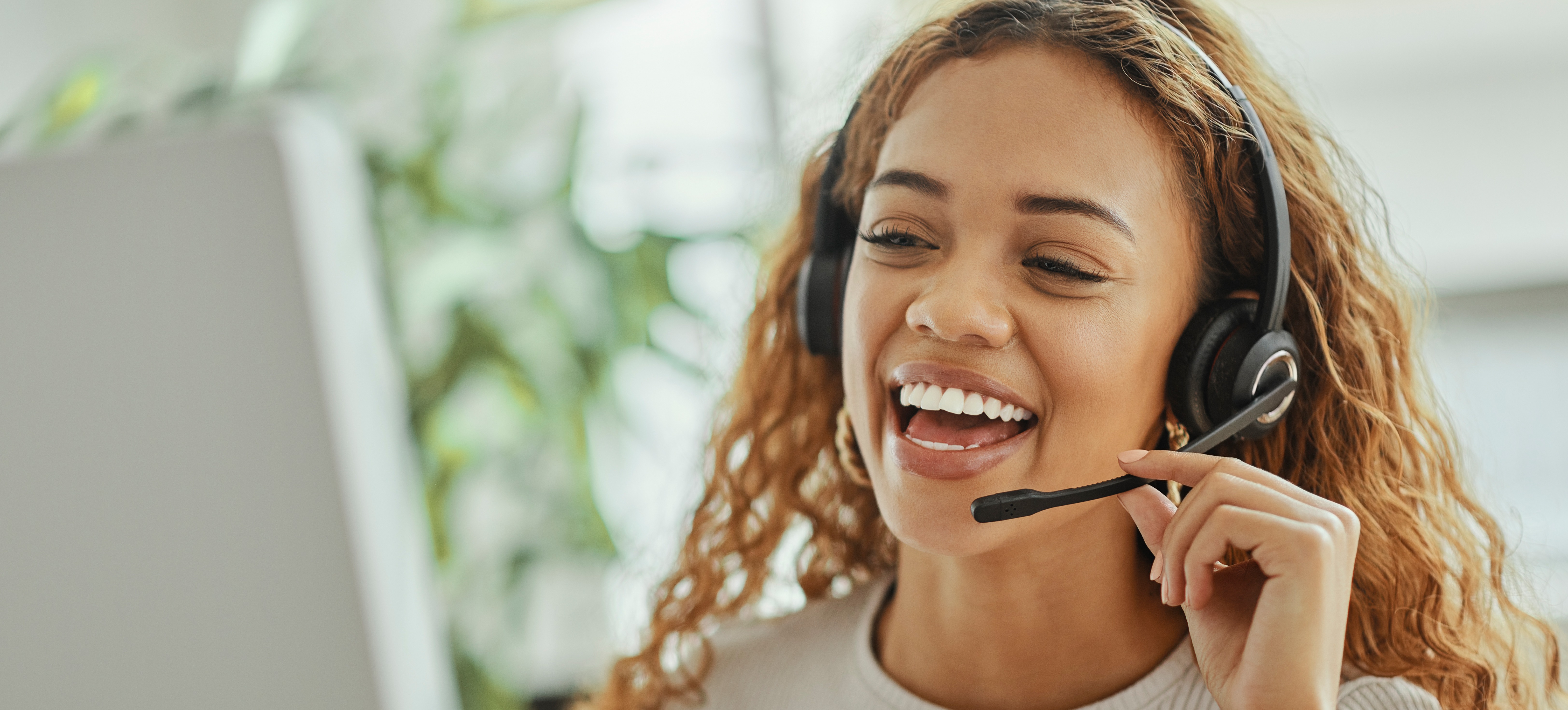 [Featured Image] A smiling woman IT support specialist talks on a headset to a customer as she looks at a desktop in front of her.
