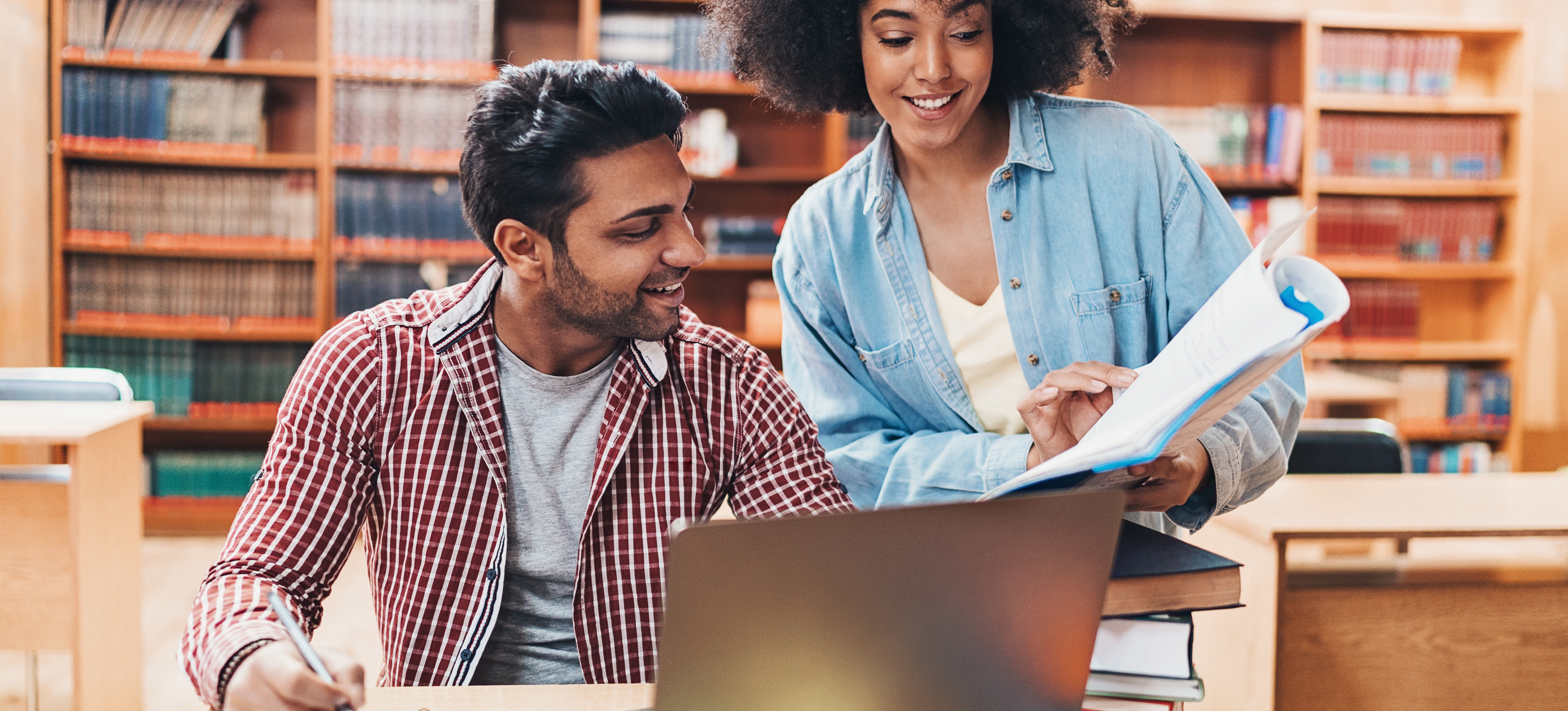 [Featured Image]: Two students in a university library discuss their data science course syllabus. 
