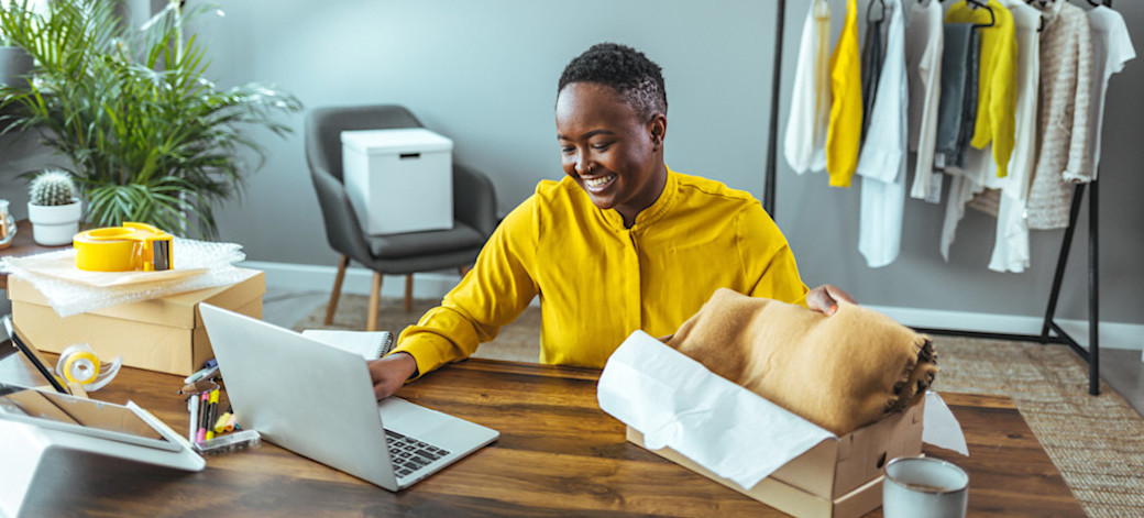 [Featured Image] A business owner sits at their shop and works on Google Ads budget management on their computer.
