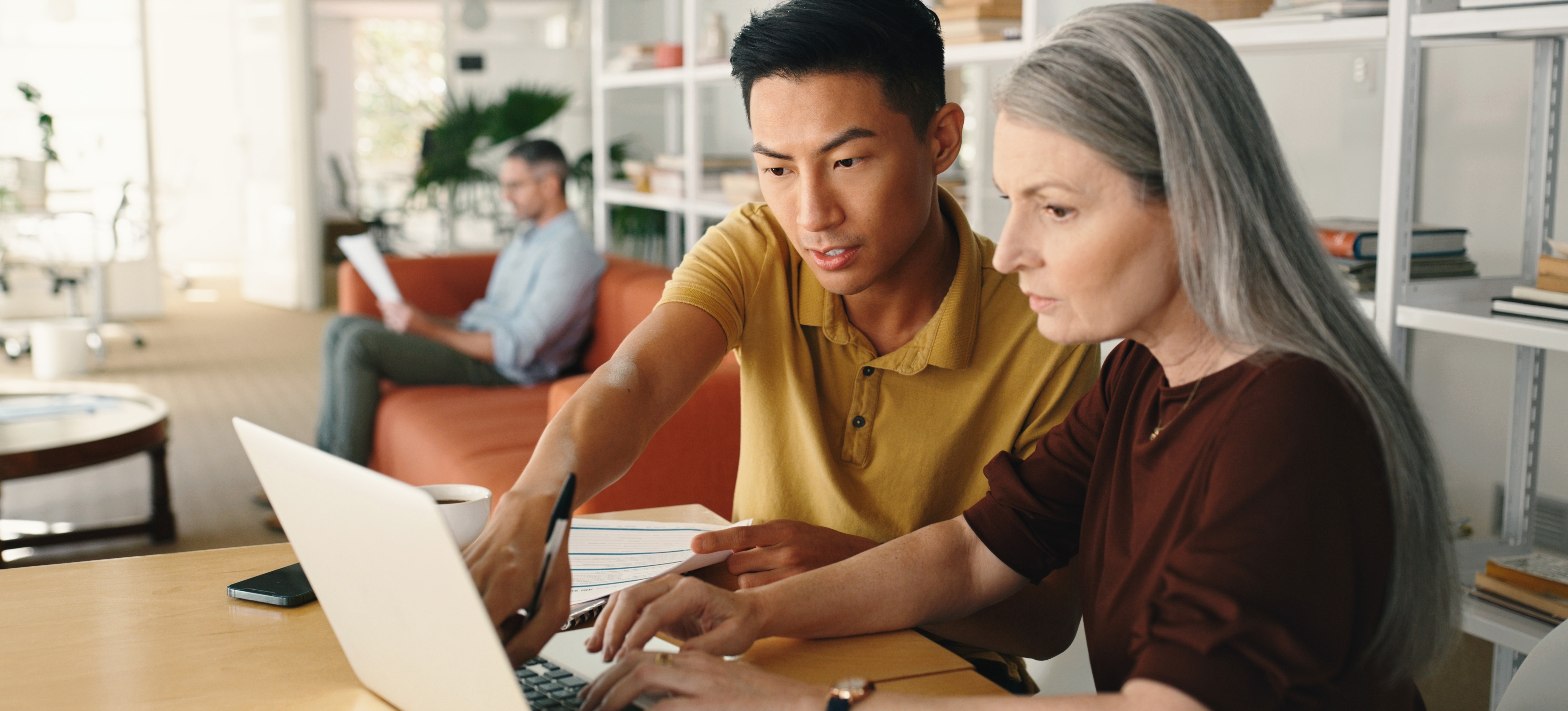 [Featured Image] A man and a women sit at a table together looking at a computer discussing the information for their blockchain project.