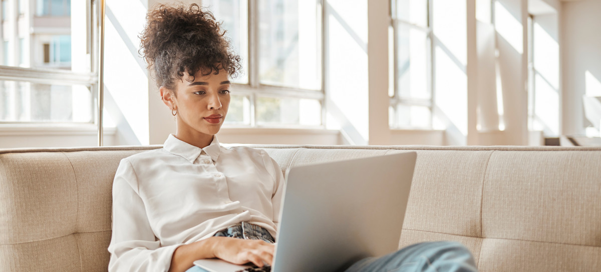 [Featured Image} A person interested in an IT career relaxes on a sofa and searches on their laptop, "What is the easiest IT certificate to get." 
