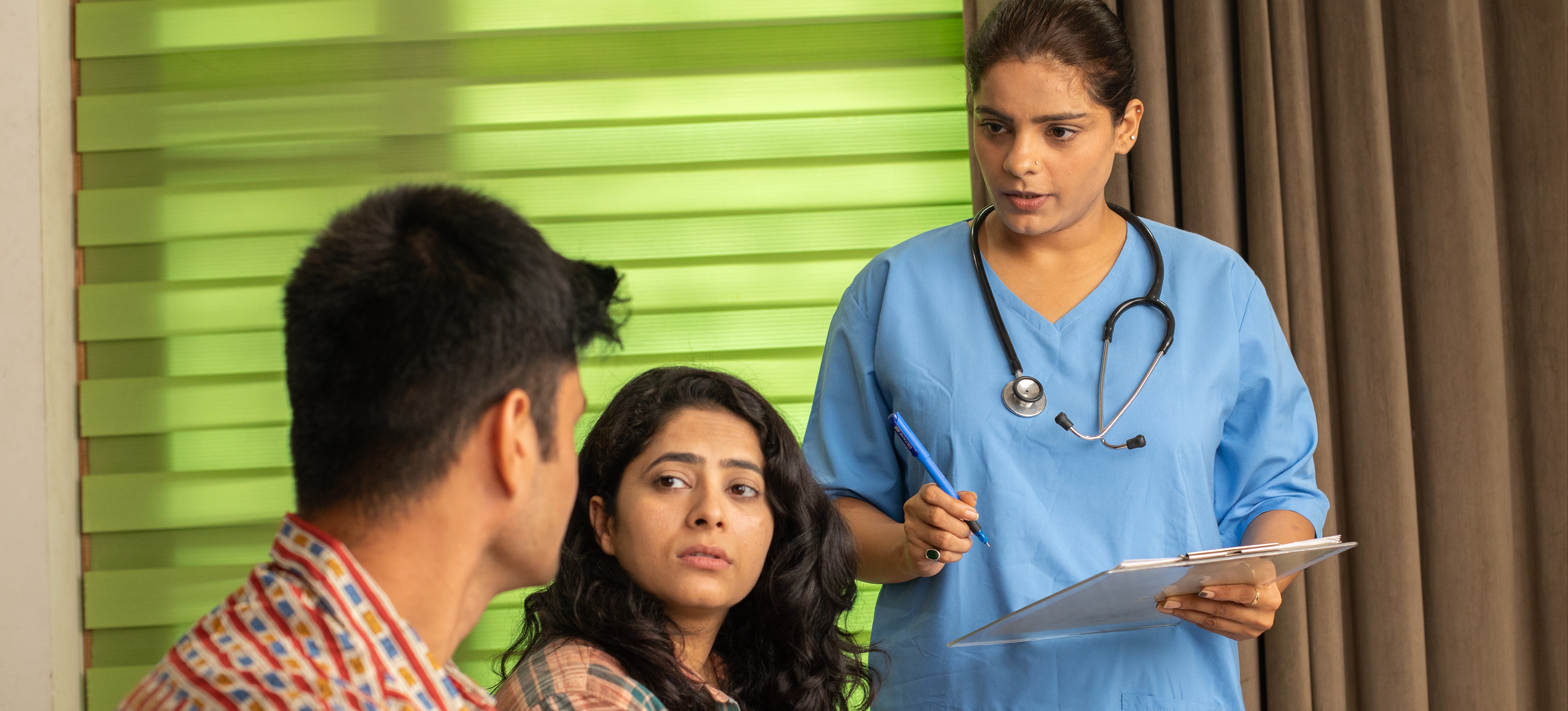 [Featured Image] A nurse speaks with two patients and records notes.
