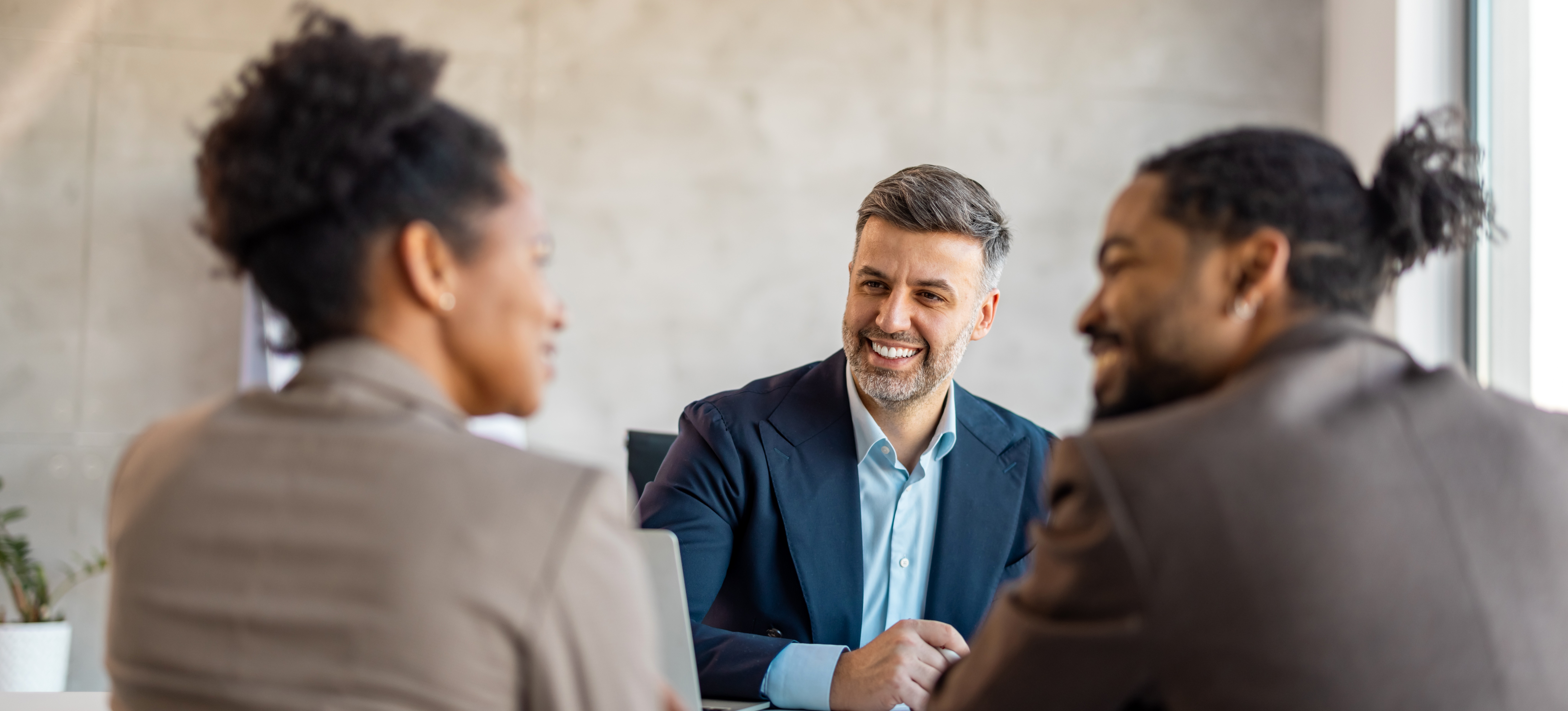 [Featured Image] A smiling sales rep who has recently received certification sits across a desk from a couple who is discussing making a purchase.
