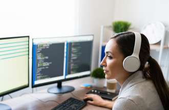 [Featured Image] A C++ programmer in white headphones uses two computer monitors to work on code for their job.
