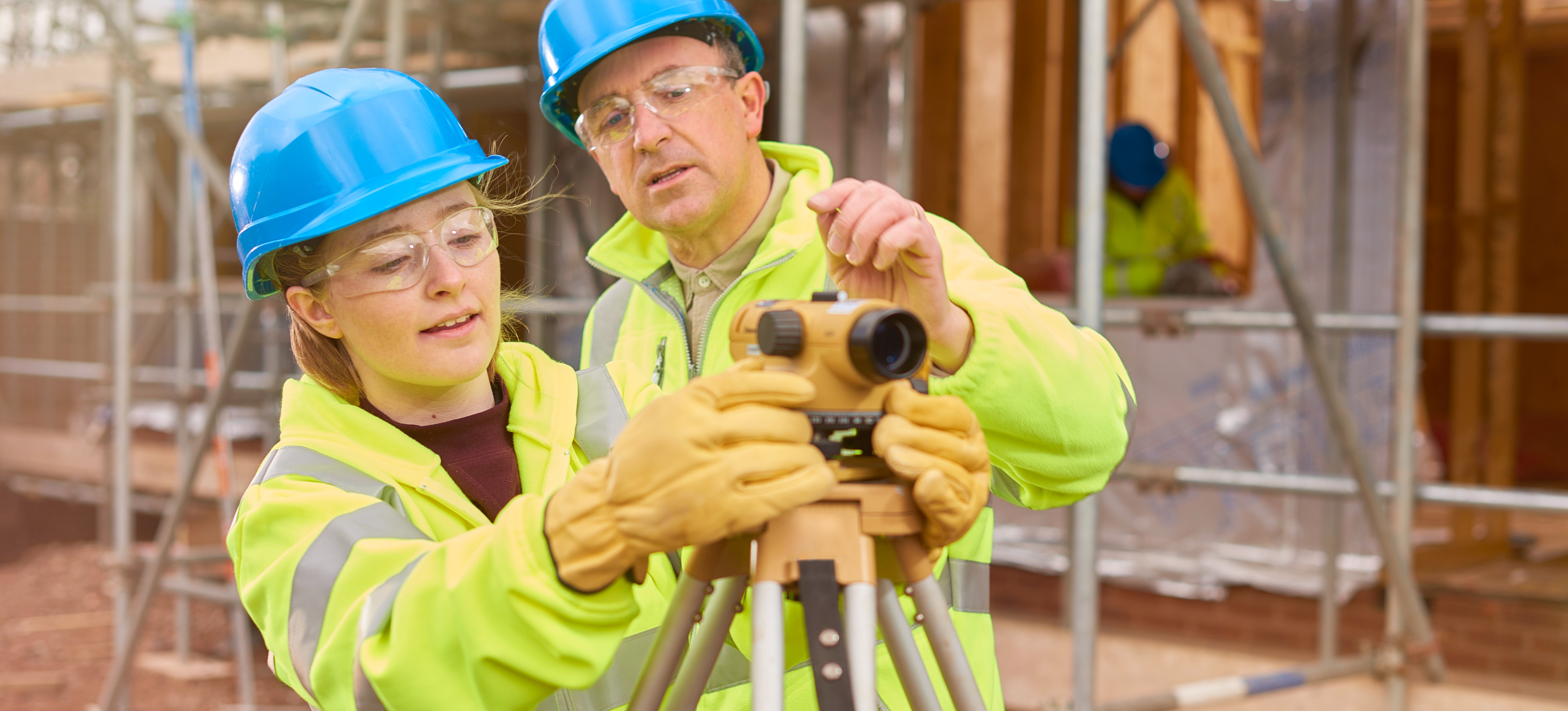 [Featured Image] A young learner in a degree apprentice program is learning how to use new technology while on a construction sight. 