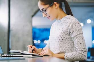 [Featured image] A female data analyst takes notes on her laptop at a standing desk in a modern office space