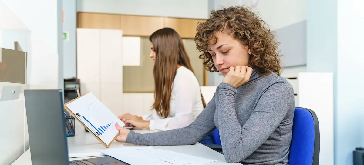 [Featured Image] Colleagues collaborating in a professional setting, analyzing printed graphs and using a computer while discussing random forest versus neural networks in AI and machine learning.
