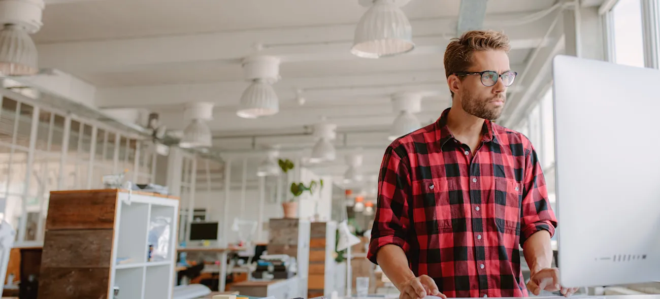 [Featured Image] An architect stands at their computer in a spacious office and works with Adobe generative AI. 
