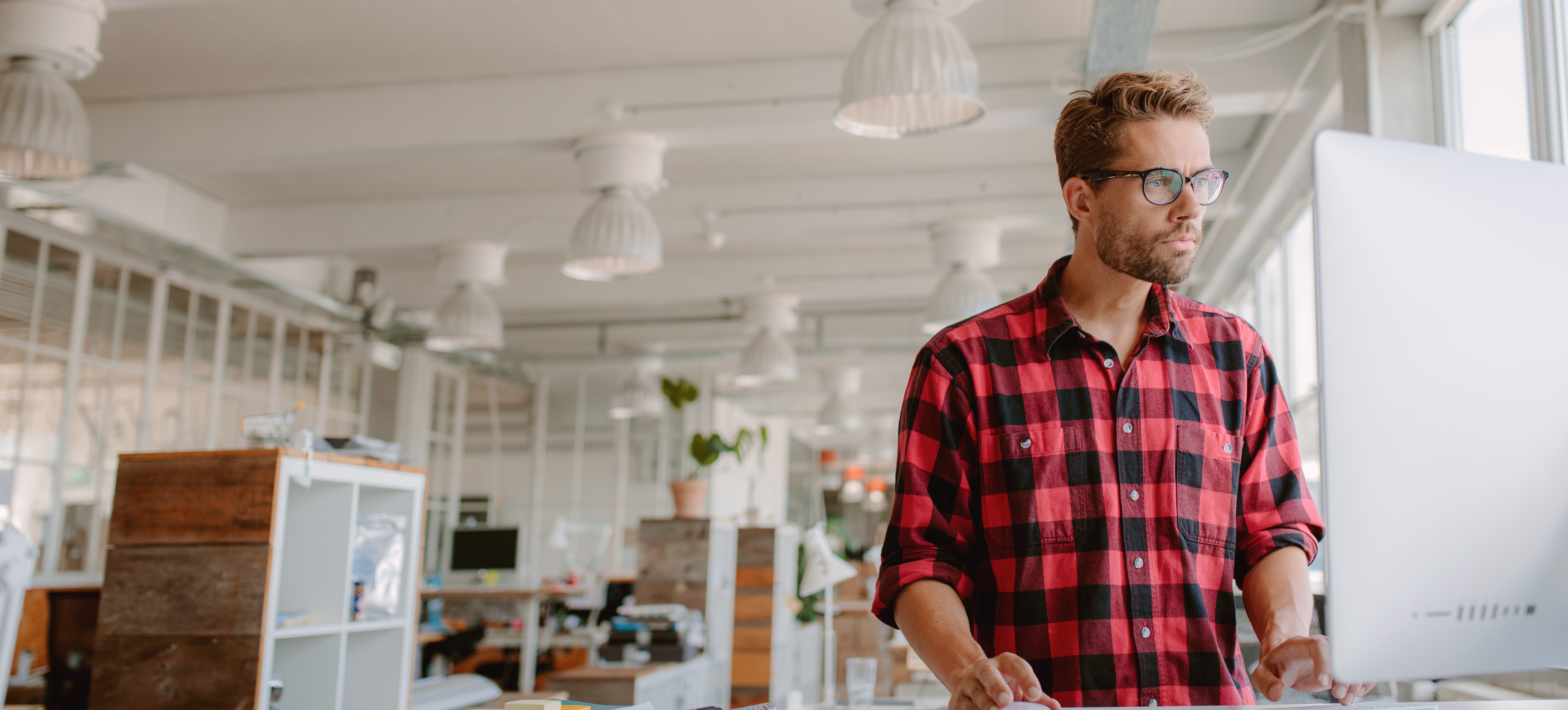 [Featured Image] An architect stands at his computer in a spacious office and works with Adobe generative AI. 
