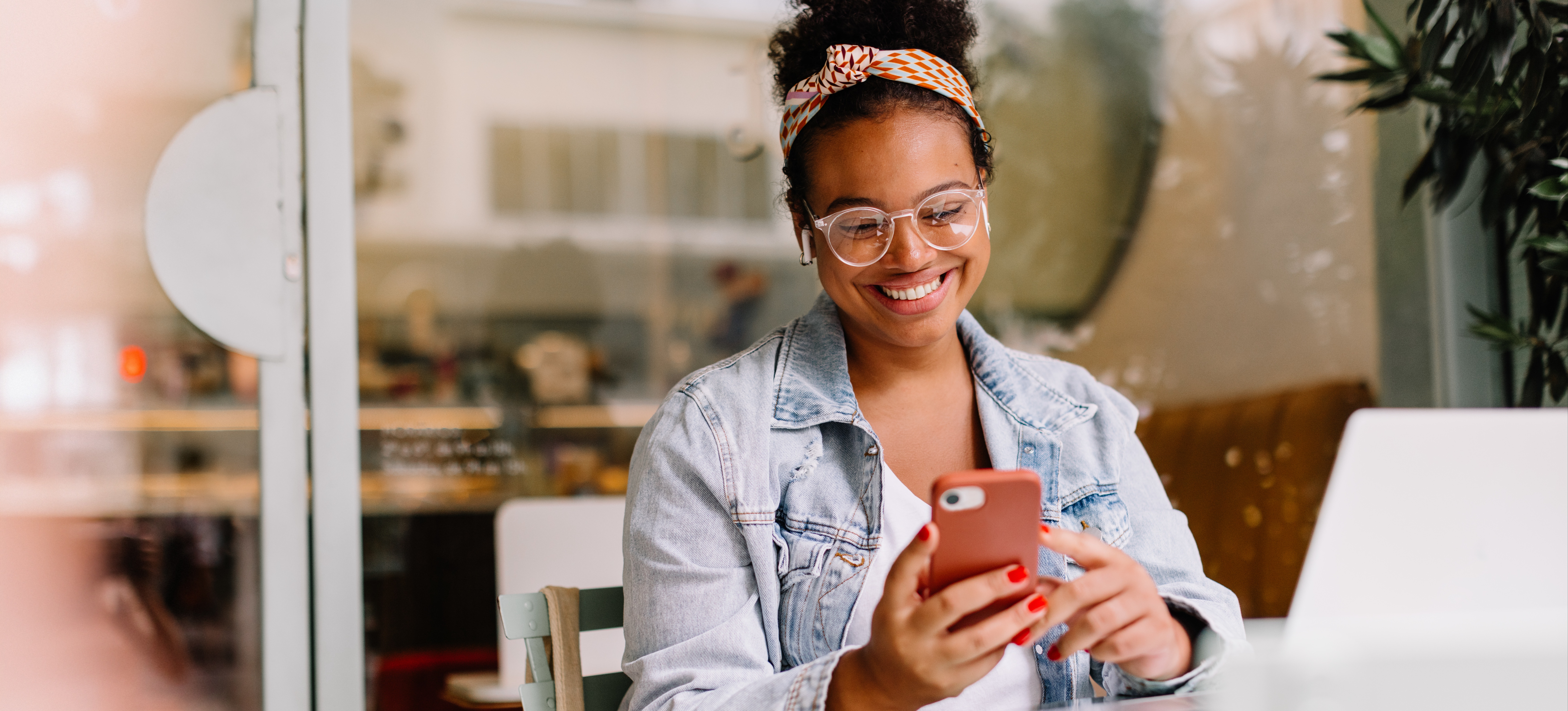 [Featured Image] A person sits at an outdoor table and looks at her iPhone to find what out what is their Mac address. 