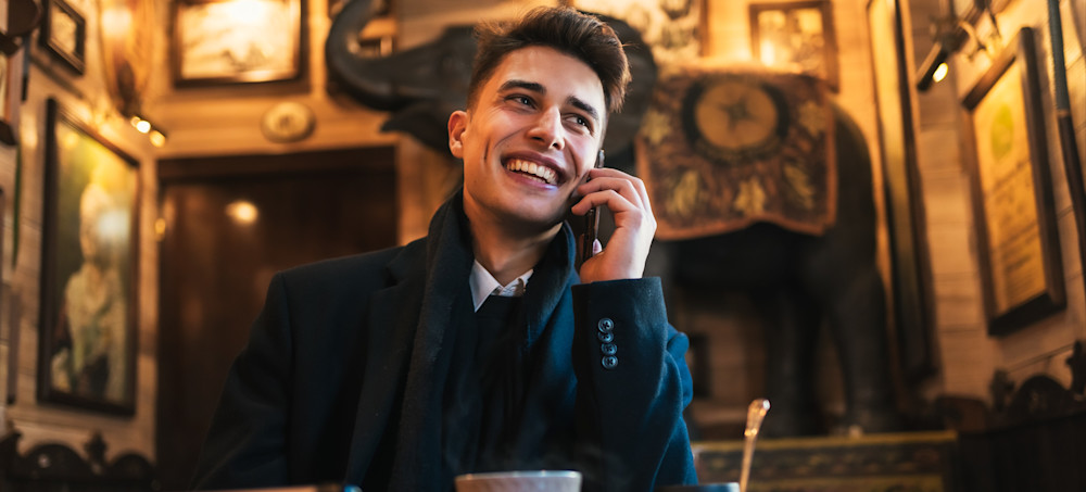 [Featured Image] A social media manager is on the phone with his client in a cafe to discuss marketing strategy