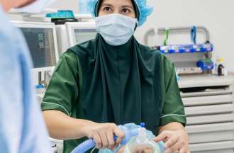 [Featured Image] A female nurse anesthetist cares for a patient in an operating room.