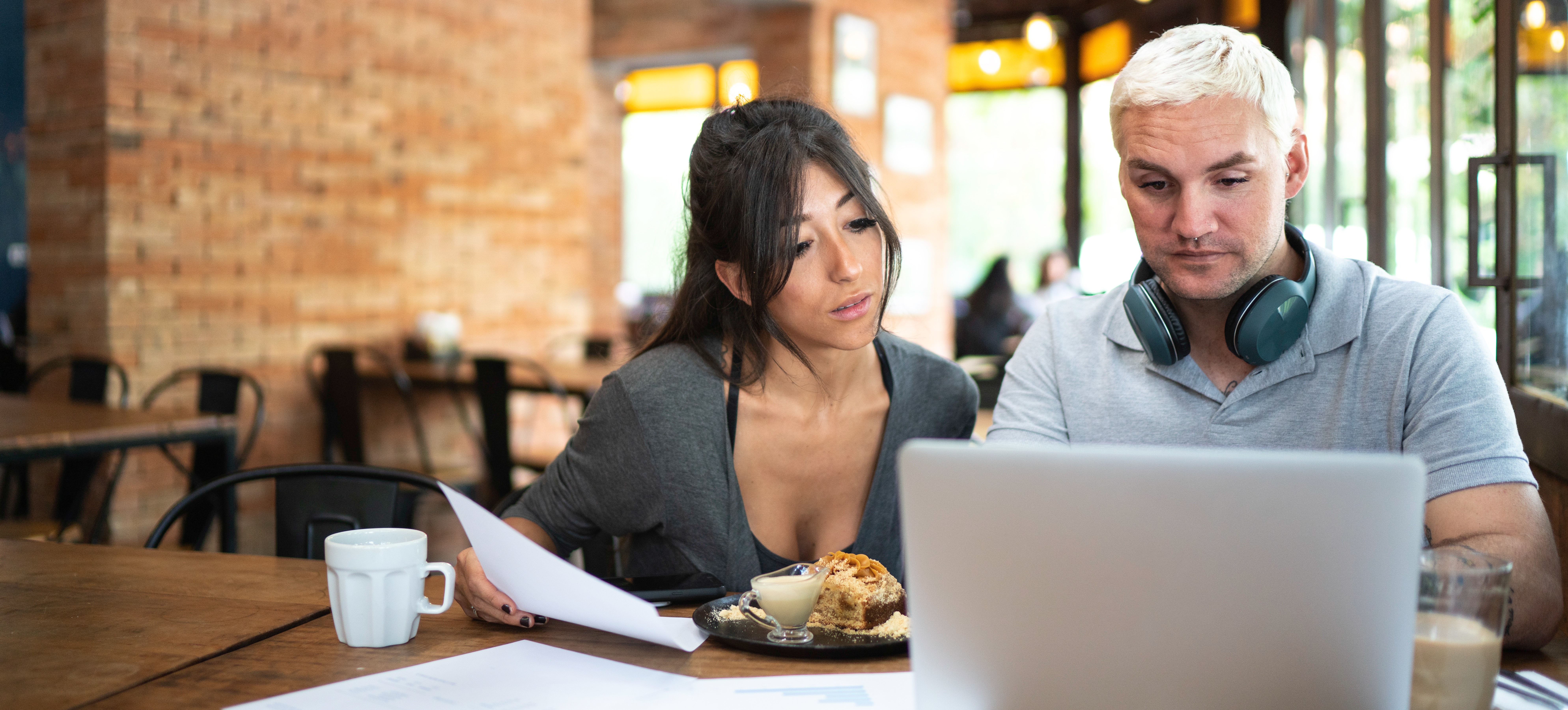[Featured Image] Two white hat hackers eat lunch in a cafe while using a laptop to try to stop a grey hat hacker's illegal activity.
