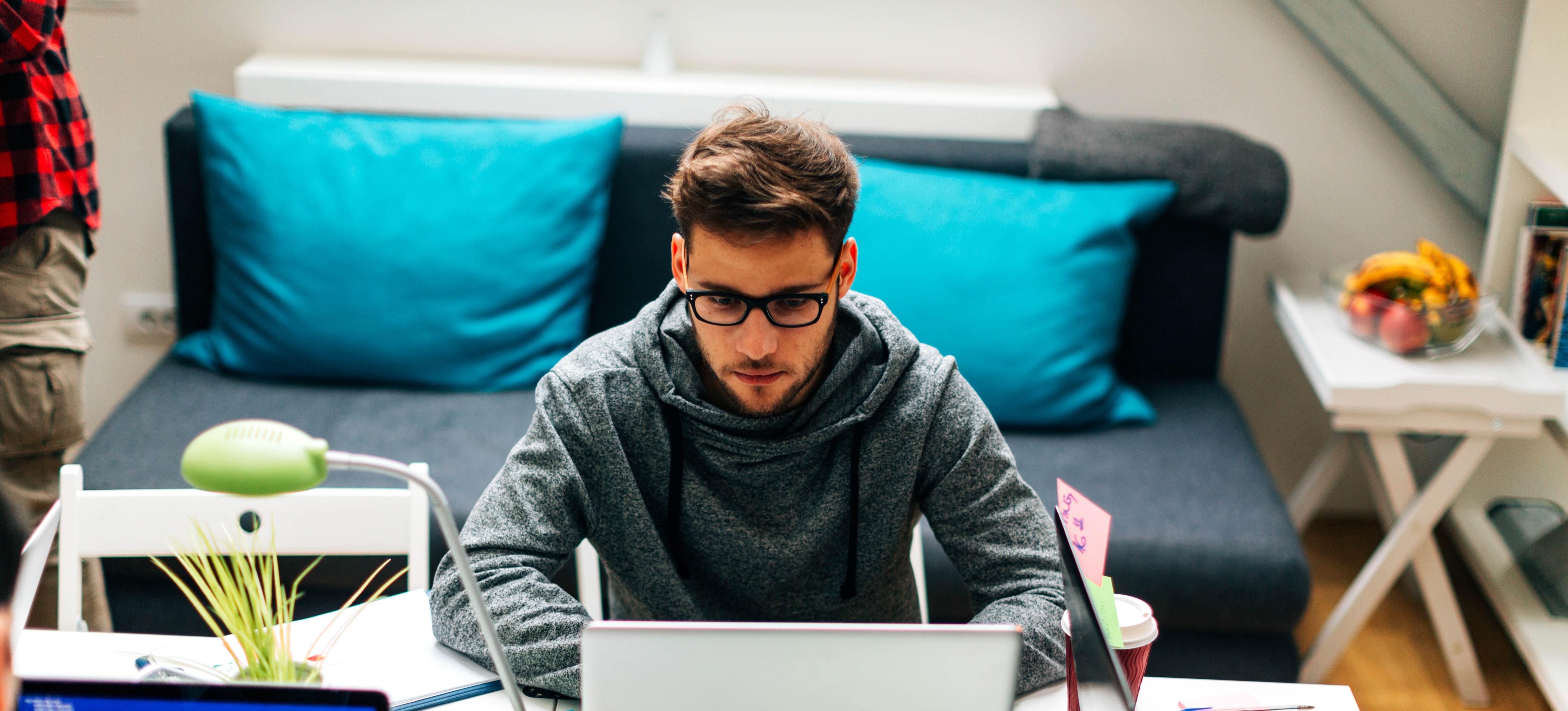 [Featured Image]:  An AI engineer with short brown hair and wearing glasses and a gray sweatshirt, is sitting at their desk working on a laptop computer.  There is another computer monitor on the desk.