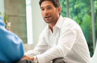 [Featured image] A loan officer in a white button-up shirt speaks with a client in a brightly light bank lobby.