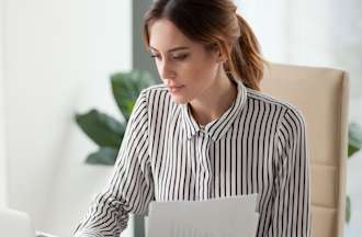 [Featured Image] A business analyst sits at a laptop and uses Power BI visualizations to create reports for her colleagues. 
