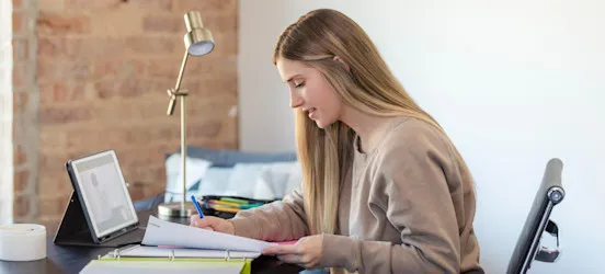 [Featured Image] Recent college graduate using a tablet and notes while adding relevant coursework to a resume.