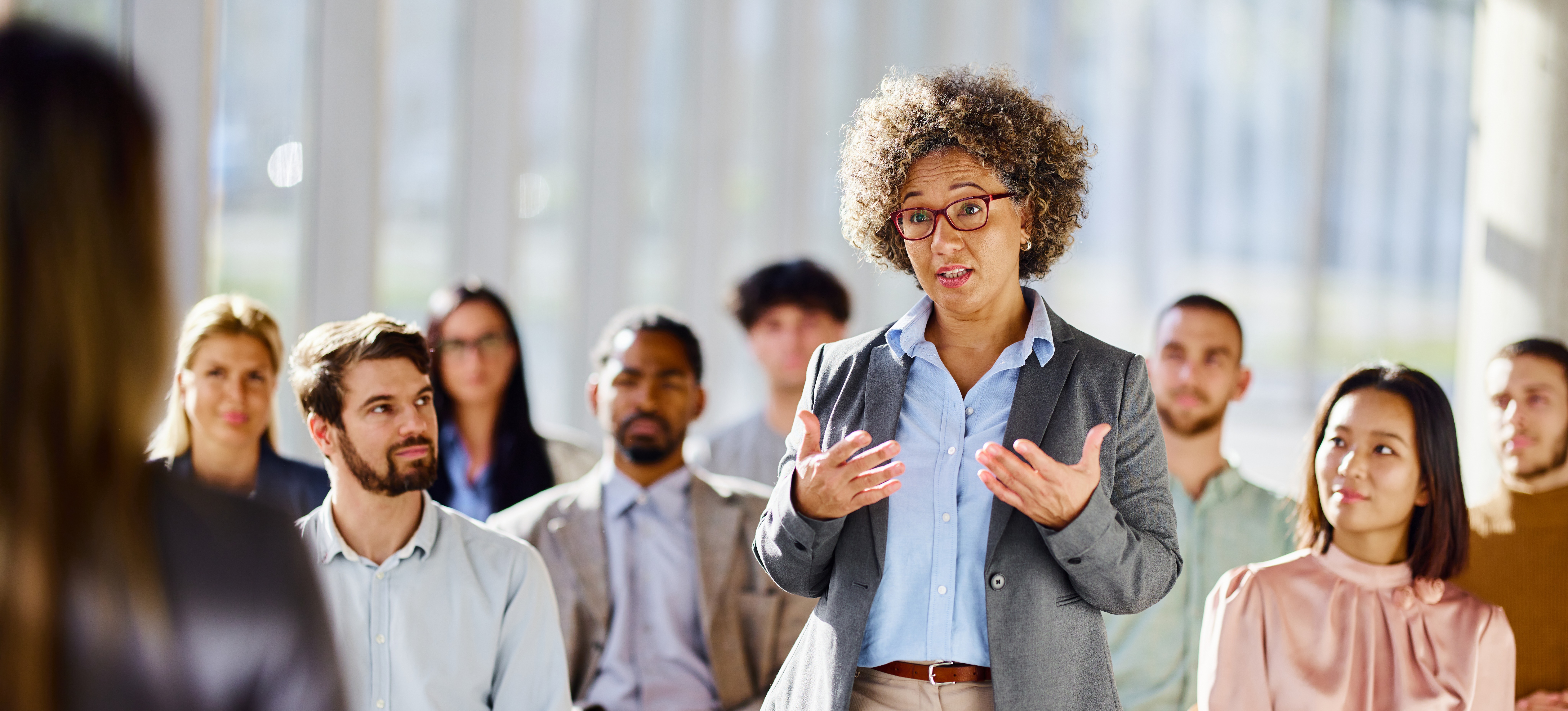 [Image en vedette] Un participant à un séminaire sur le développement organisationnel se tient debout et s'adresse au présentateur dans une salle remplie de professionnels assis sur des chaises.