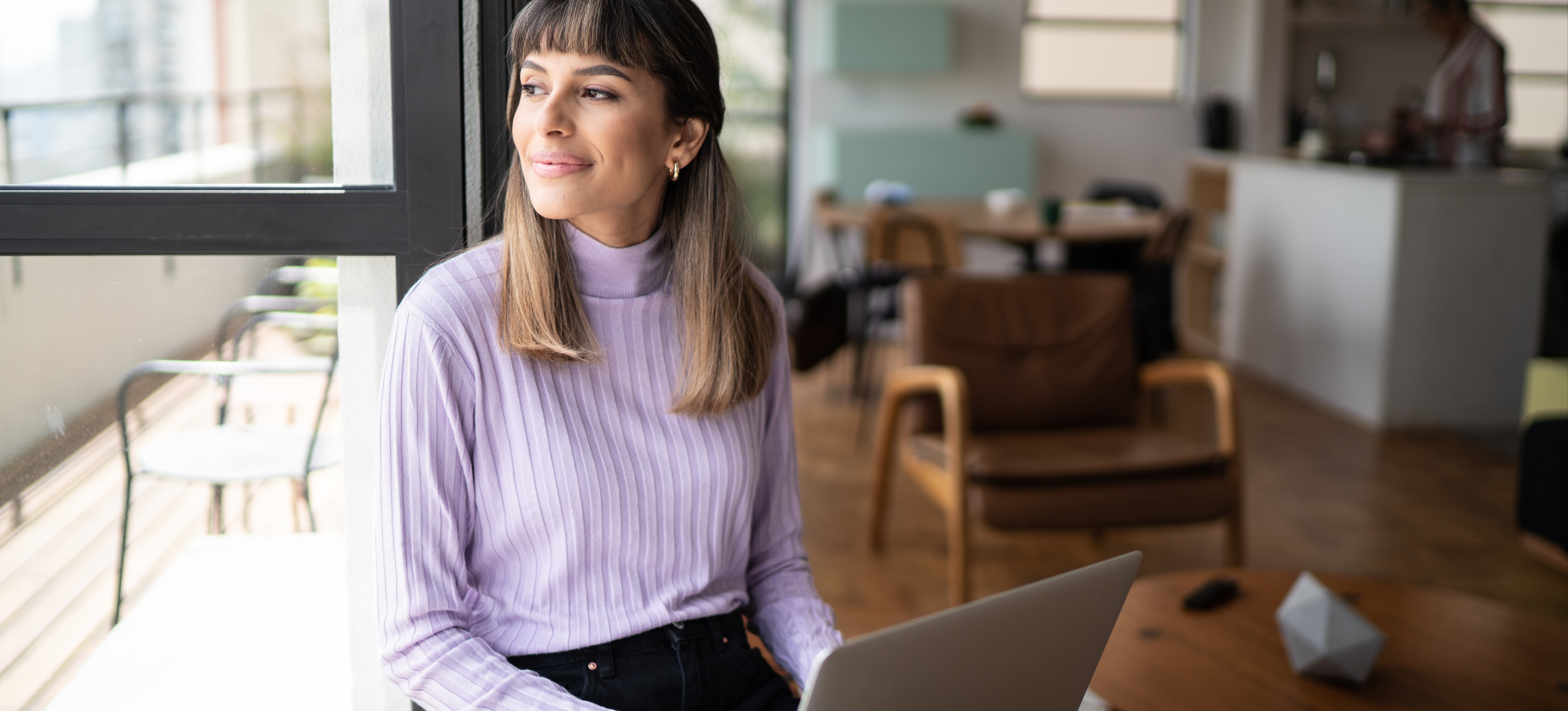 [Featured Image] After applying strategies for overcoming imposter syndrome, a professional woman sits with her laptop while in the office.