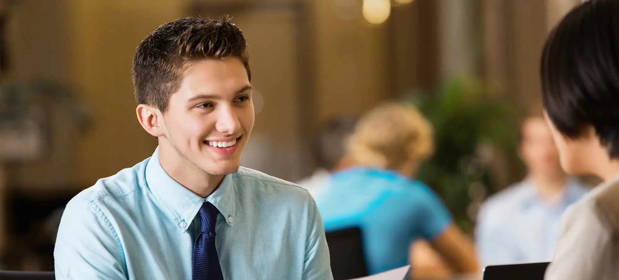 [Featured Image]: A job applicant in a shirt and tie talks to a hiring manager while holding his CV.