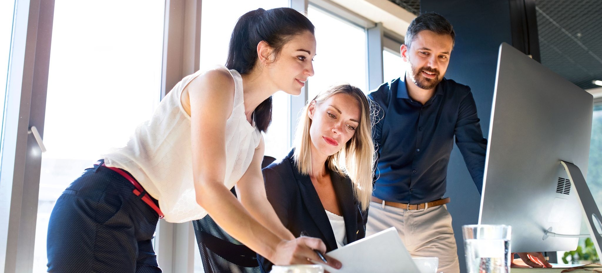 [Featured Image] Three coworkers are using their job skills to collaborate as they assess papers and look at a computer screen. 