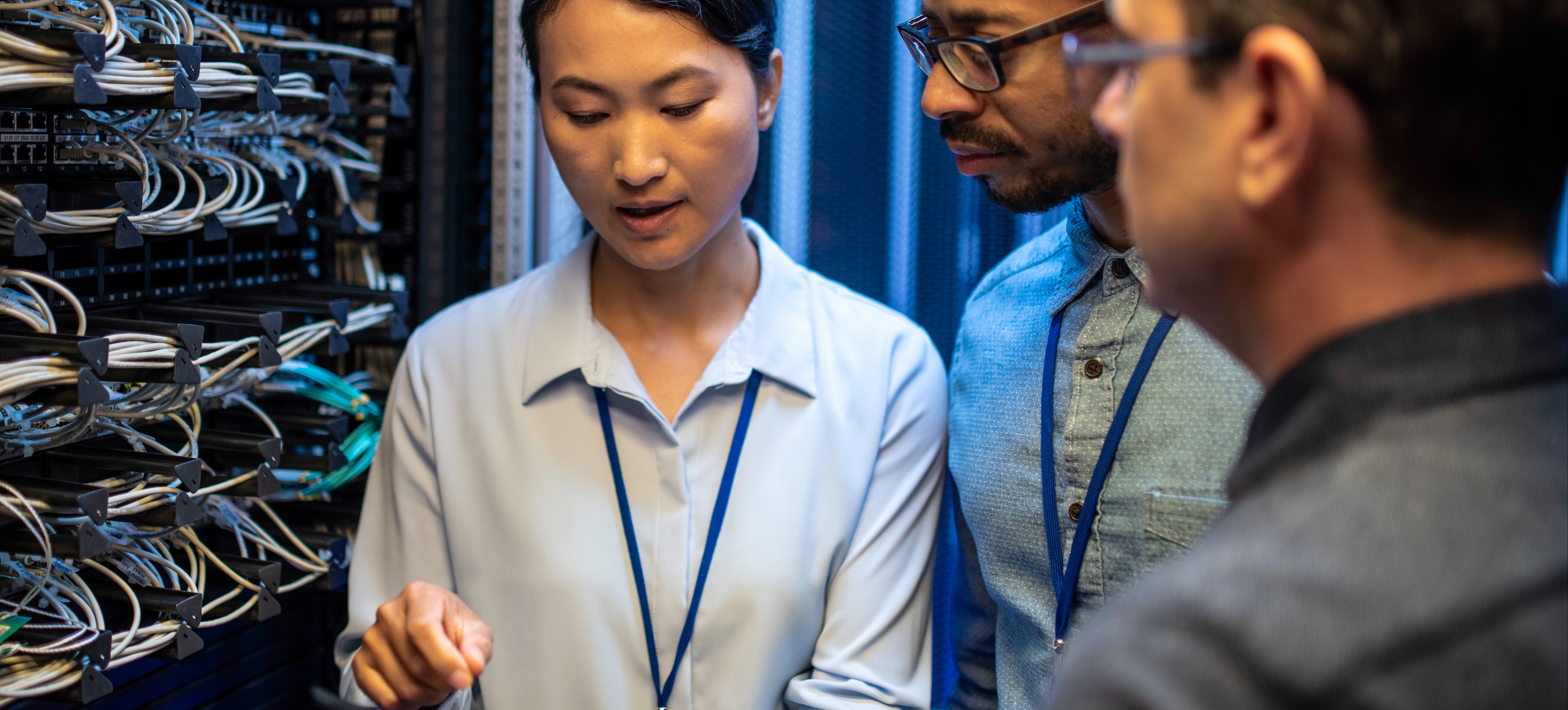[Featured Image] Three mainframe developers looking at a digital tablet and talking while standing next to a server in a data center.