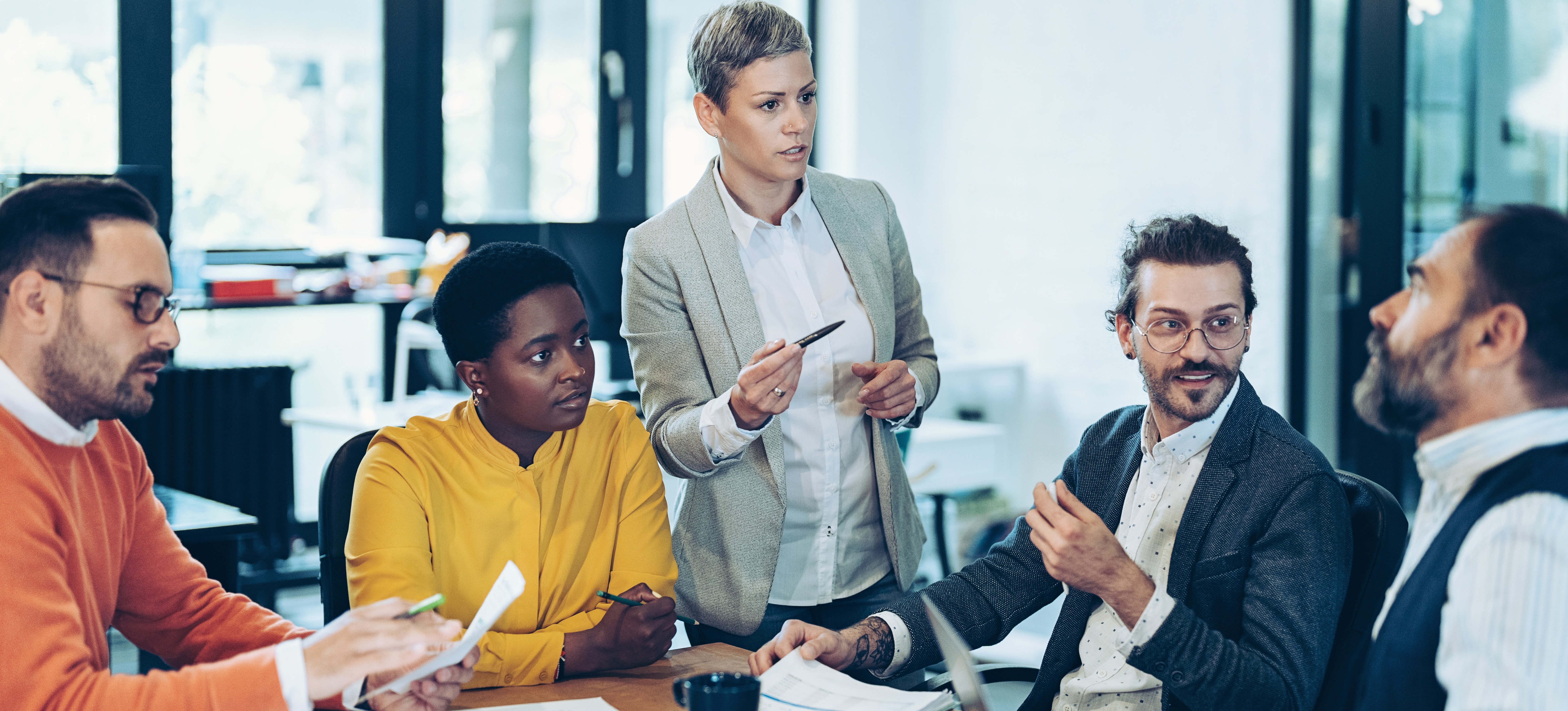 [Image en vedette] Un groupe de professionnels certifiés PMP discutent de leur projet autour d'une table dans un lieu de travail spacieux.
