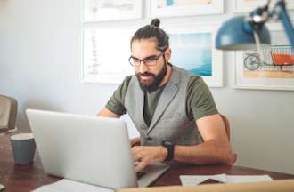 [Featured Image] A man works on a laptop at a desk. 