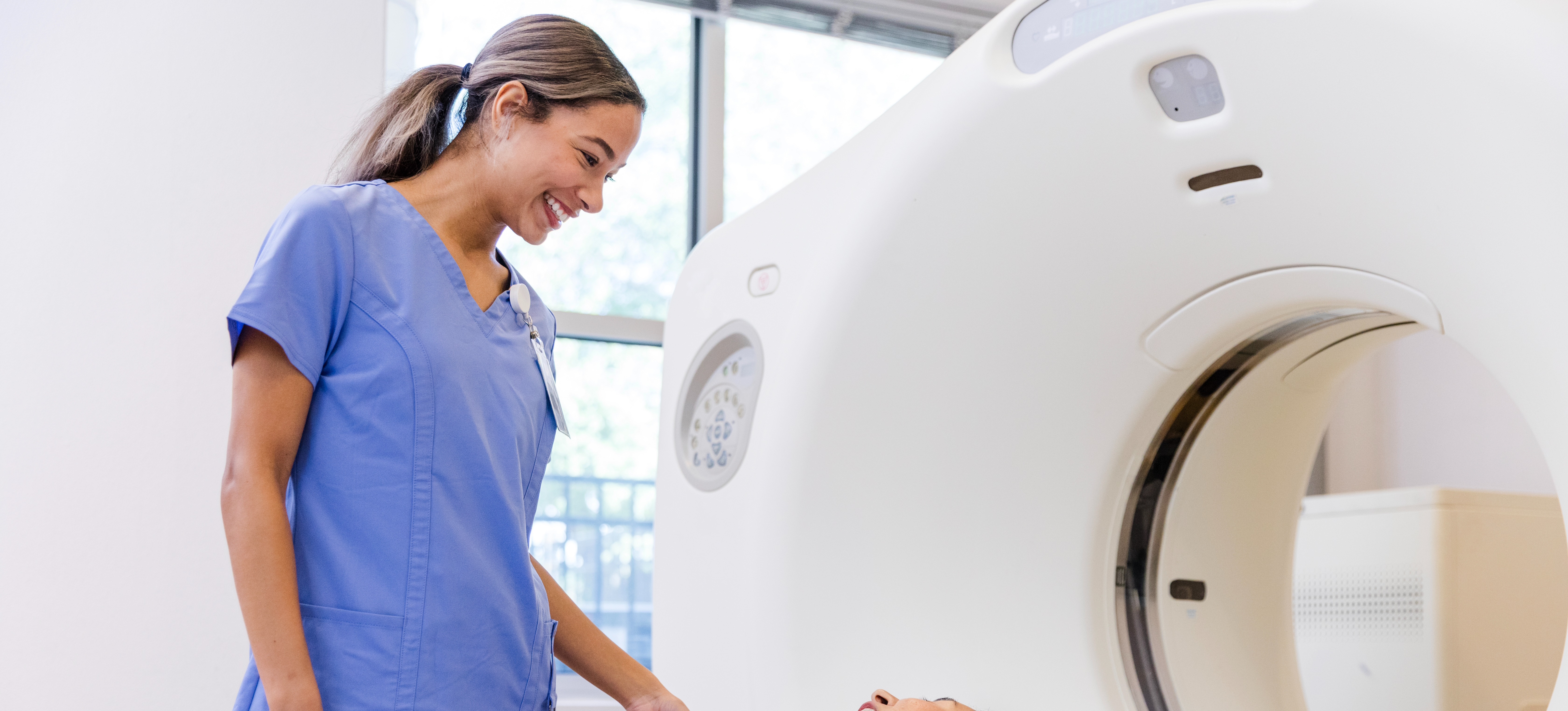 [Feature Image] An MRI technologist smiles while preparing a patient for their imaging test.
