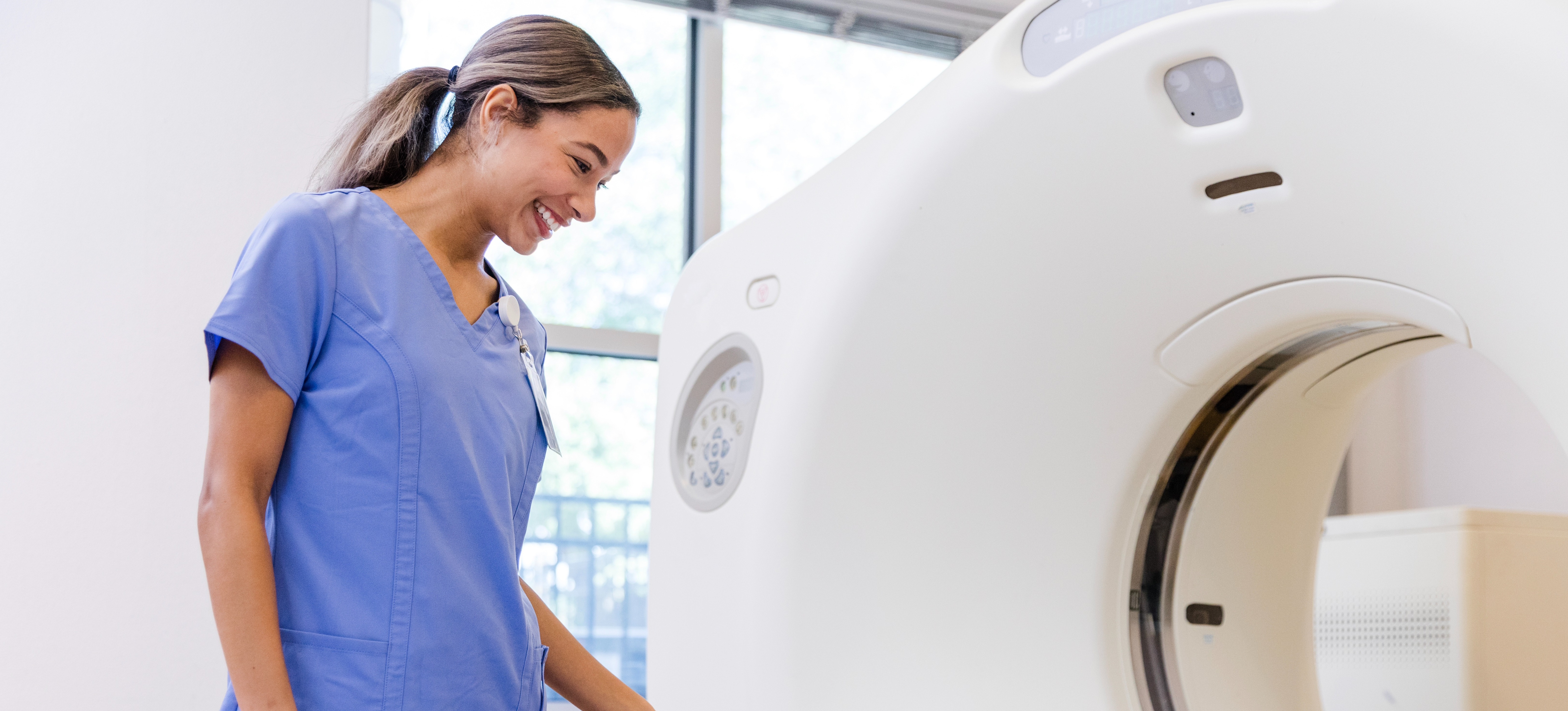 [Feature Image] An MRI technologist smiles while preparing a patient for their imaging test.
