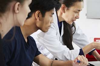 [Featured image] Three people look at a computer. One has a lab coat on.