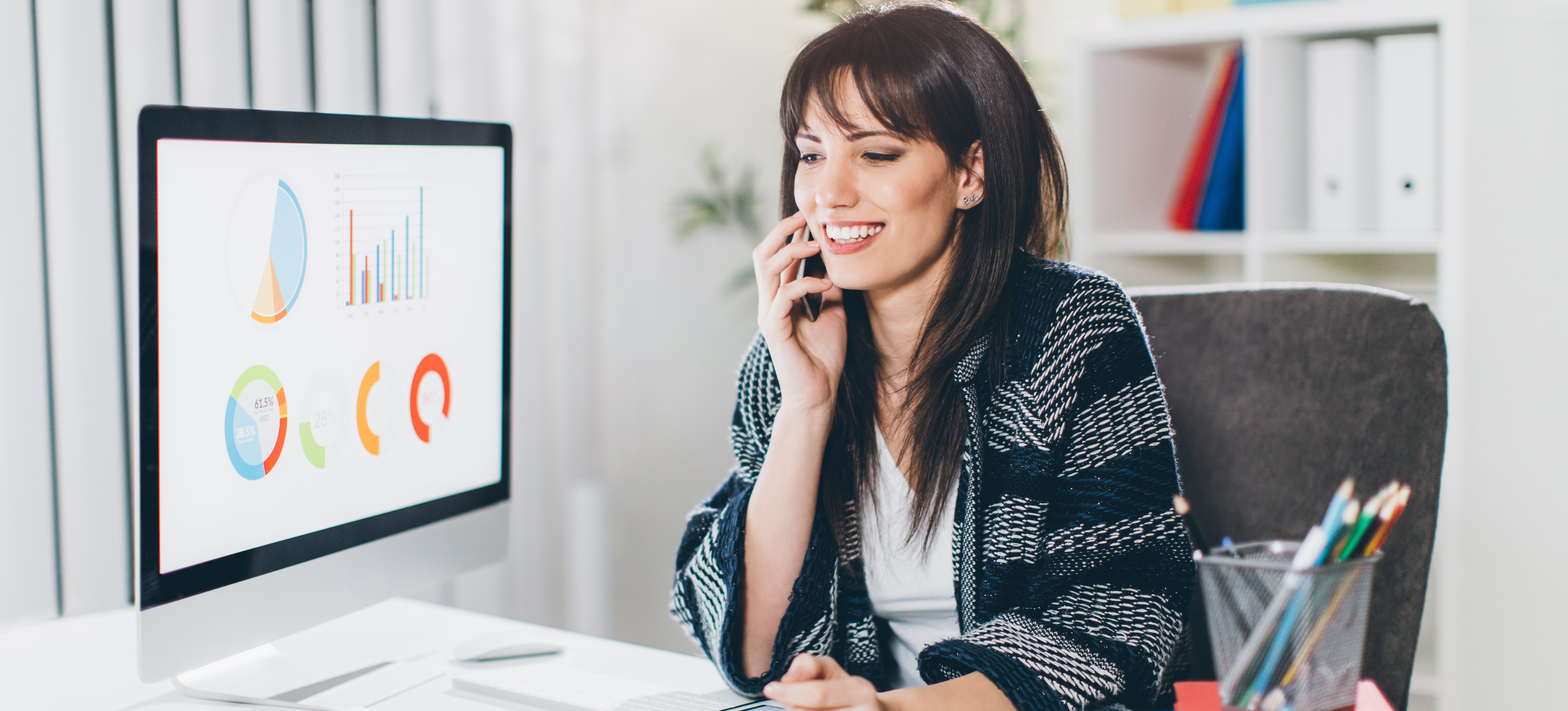 [Featured image] An e-commerce specialist talks on the phone at their desk while looking at data on a computer. 
