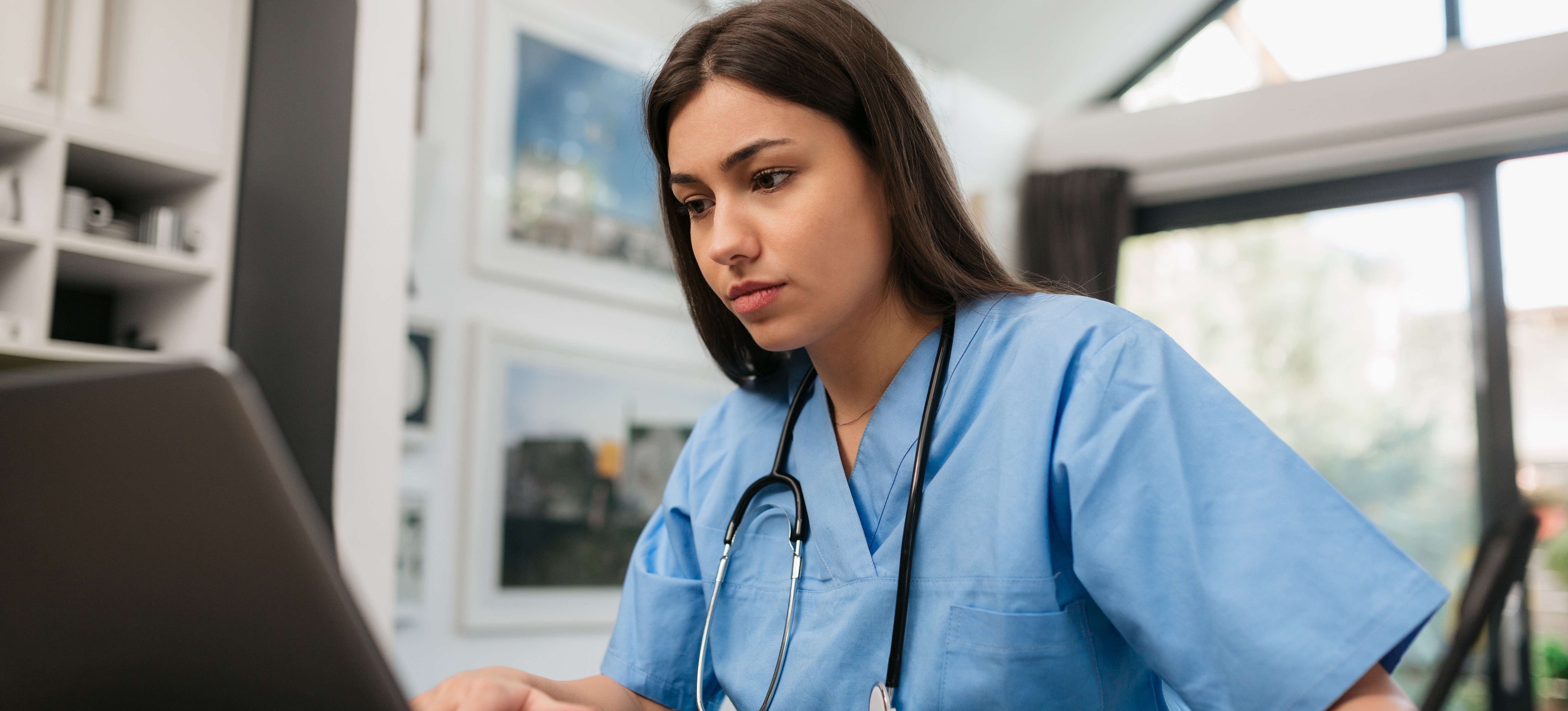 [Featured Image] A young professional is on a laptop at home, taking online classes to get a degree in nursing.