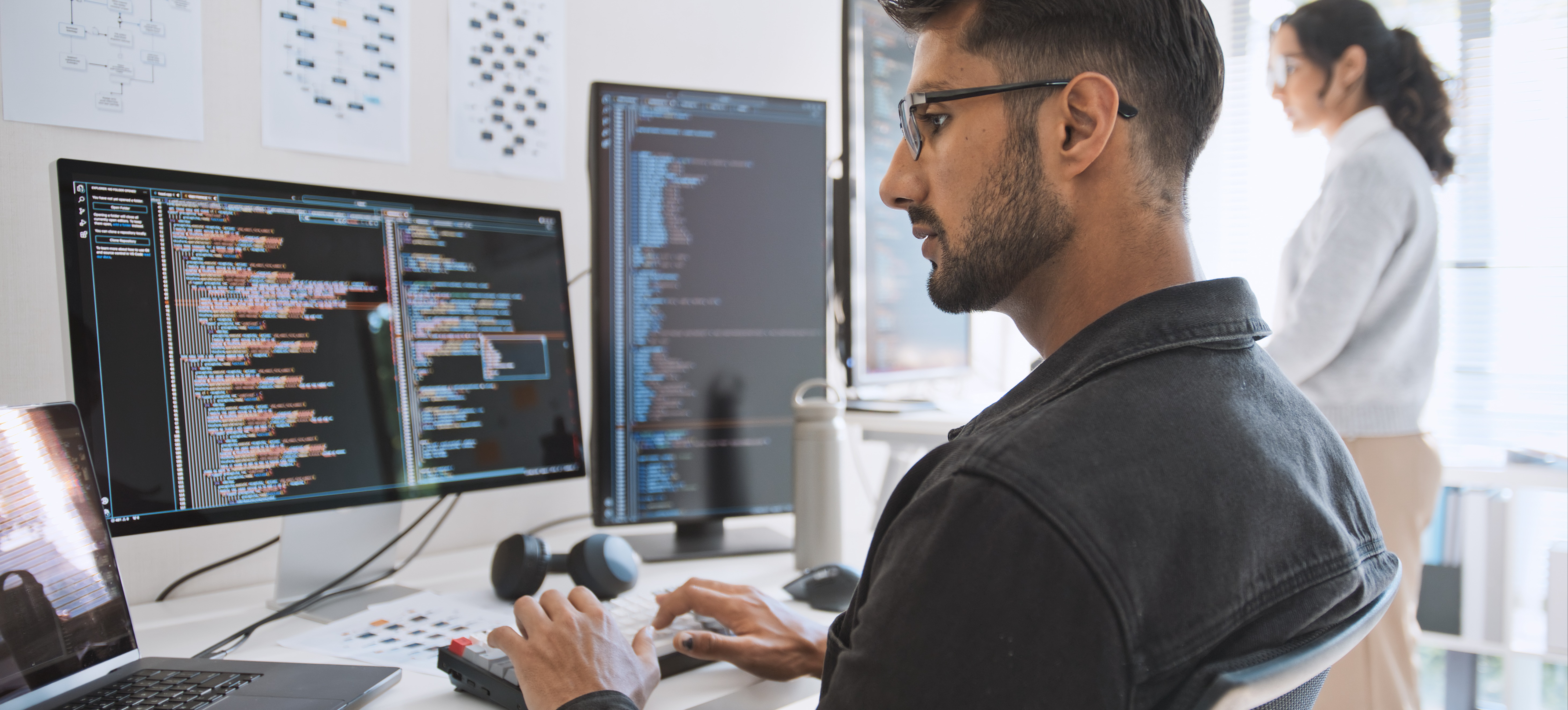 [Featured Image] Two colleagues study code on large computer screens, using cloud security tools to help protect their organization’s cloud data.
