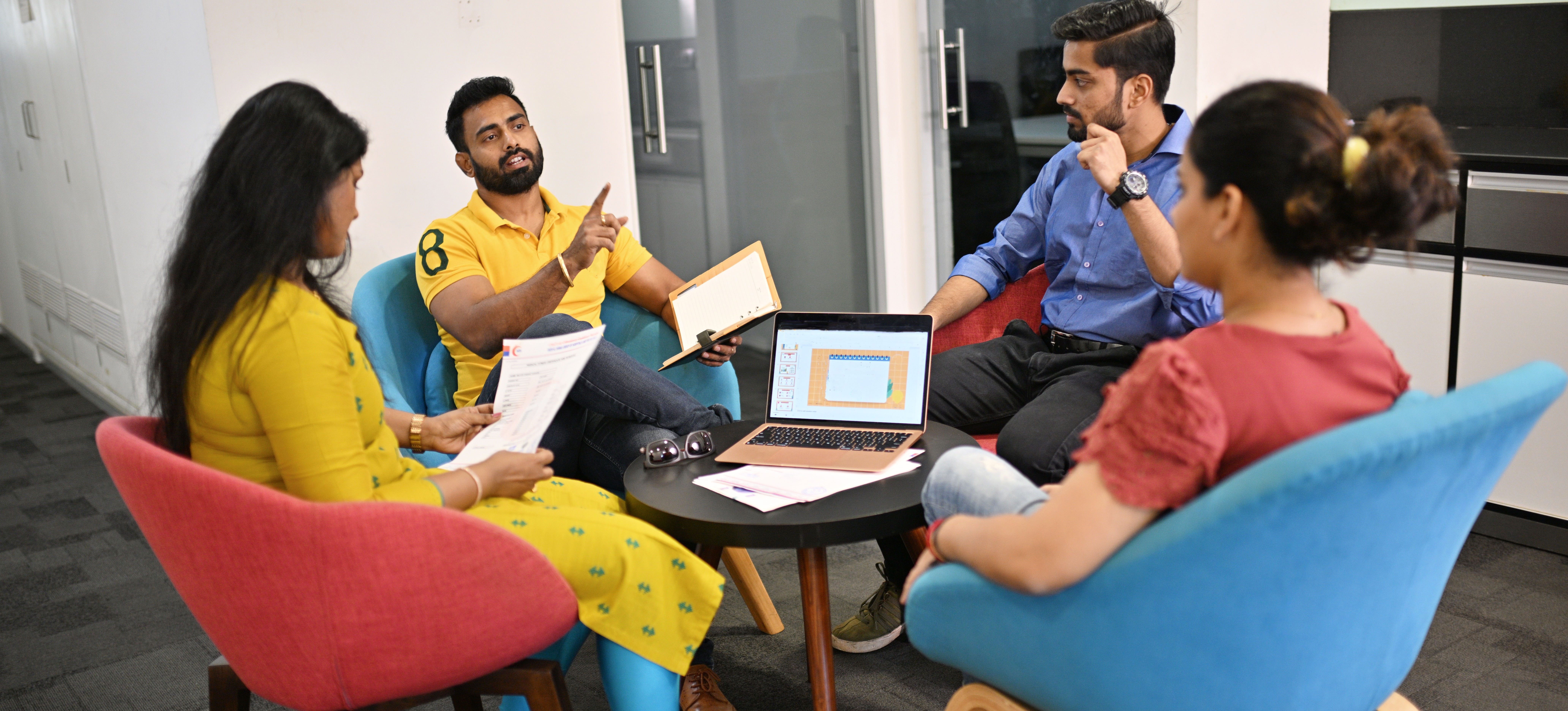 [Featured Image]: Four people sit around a table talking as they engage in project planning.
