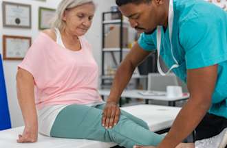 [Featured Image] A phsyical therapy assistant ewaring scrubs works with a patient. 