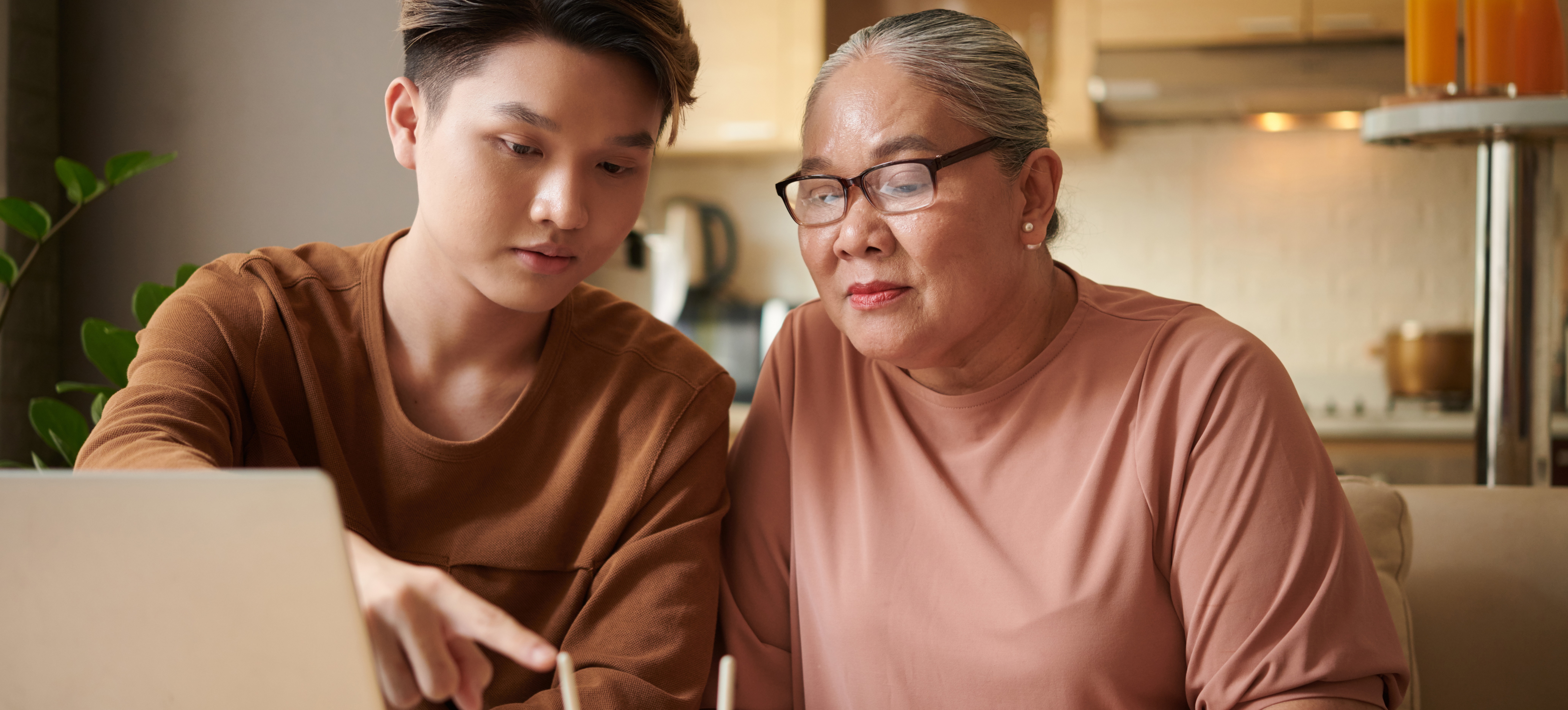 [Featured Image] An older women sits with her younger grandson at a table asking "what is a router?" He is showing her how a router works.