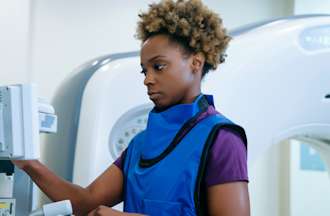 [Featured Image]: A radiation therapist works with equipment while wearing a blue safety vest.