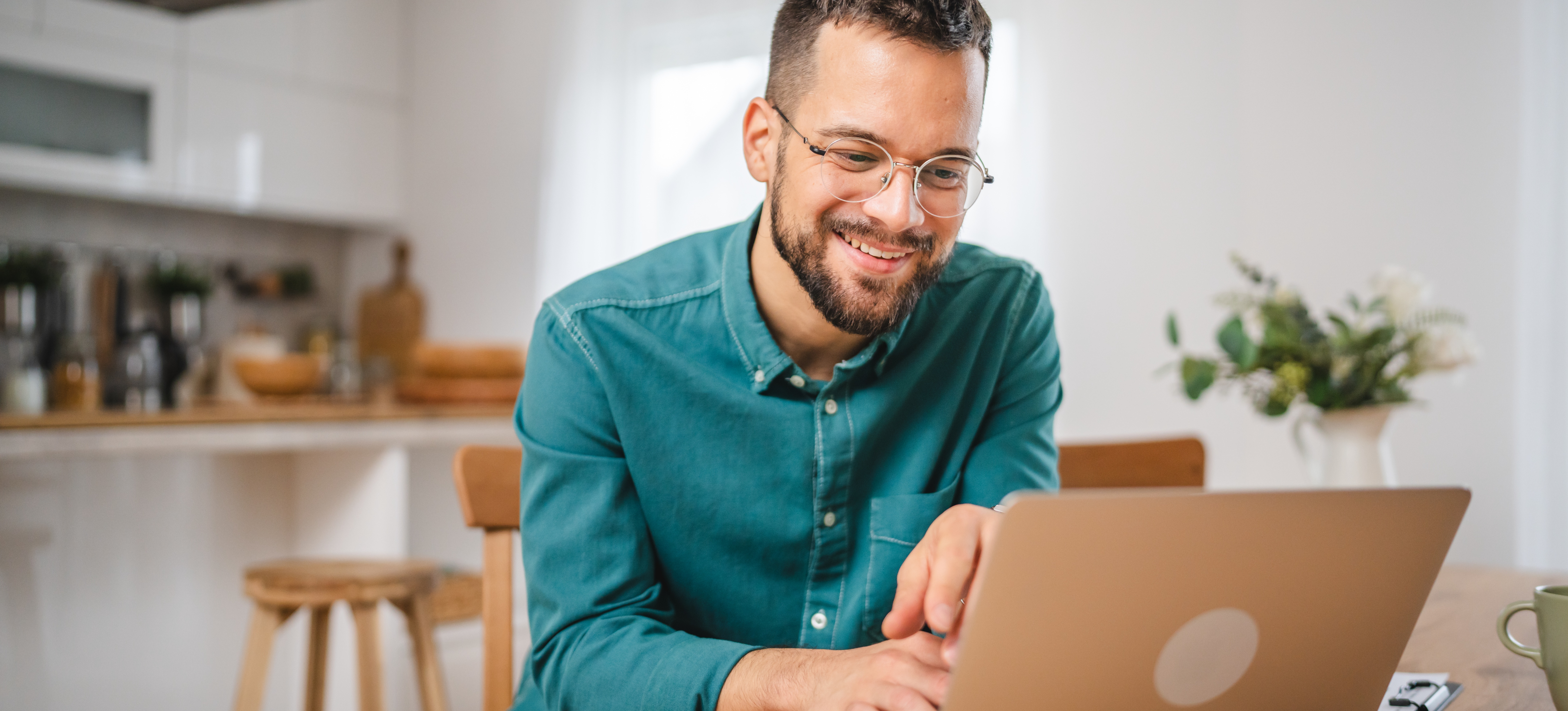 [Featured Image] A man sits at his table at home with his laptop. He is researching how to buy cryptocurrency.