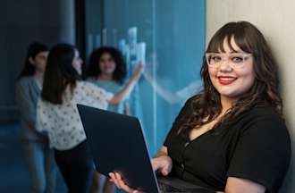 [Featured image] A business analyst stands in an office hallway holding a laptop computer as they prepare for a meeting.