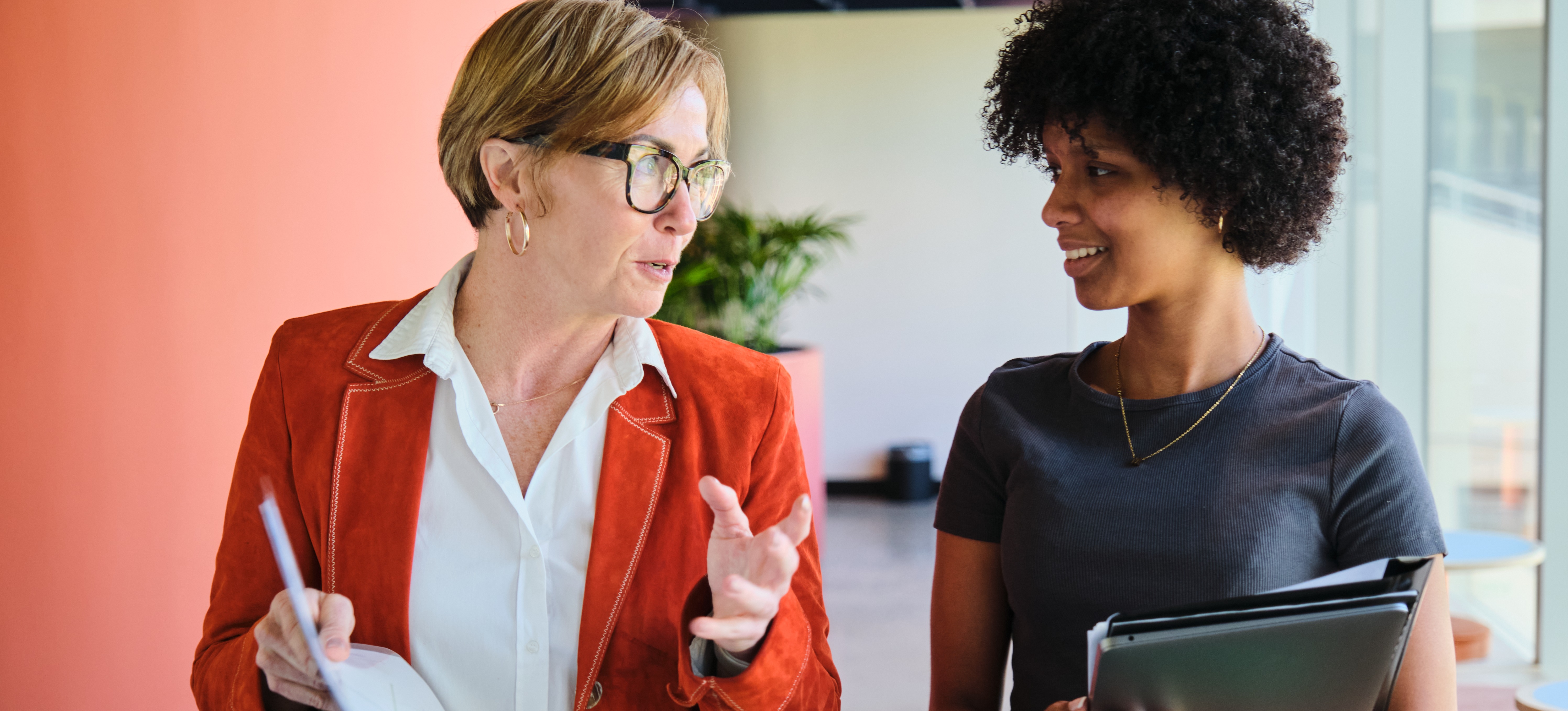 [Featured Image] Two colleagues walk through their office and discuss their company's SWOT analysis.   