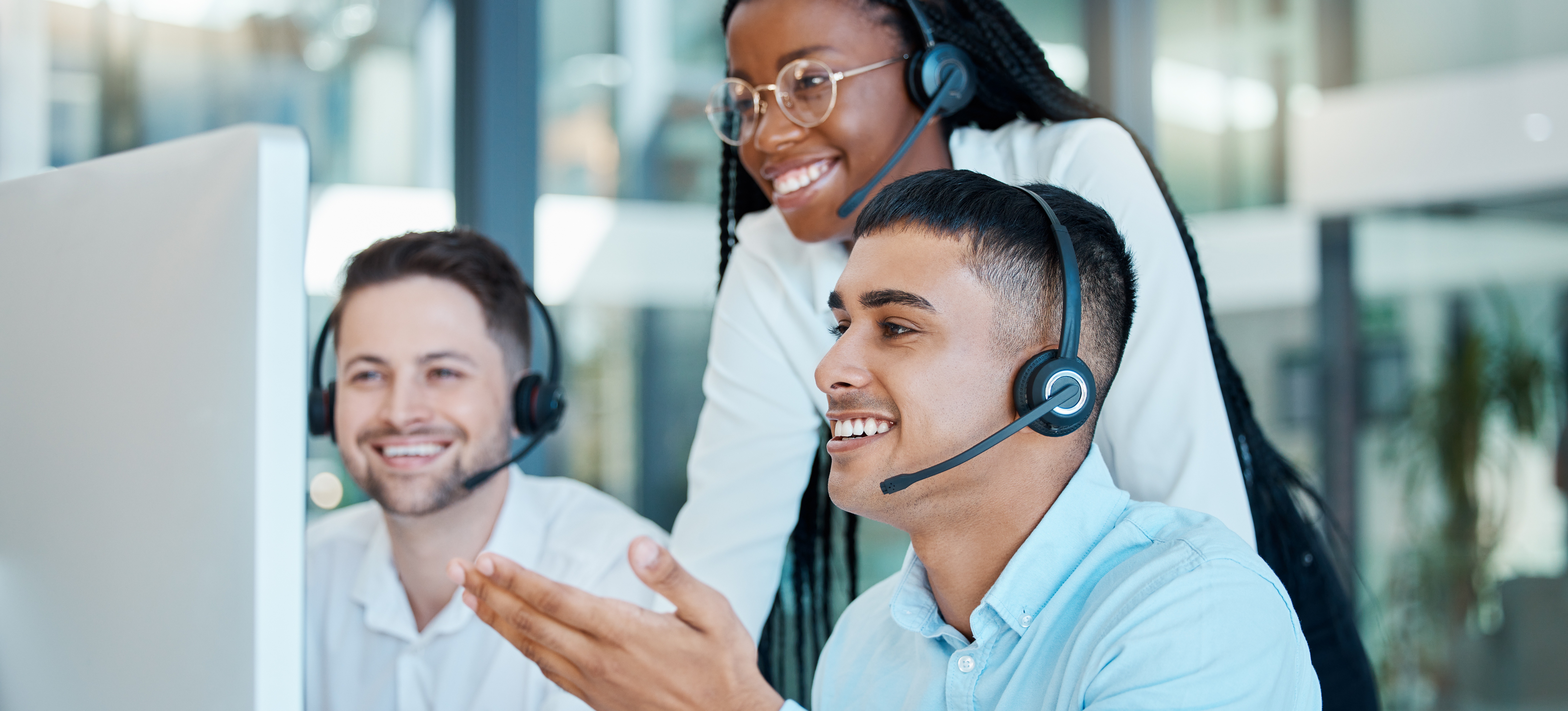 [Featured Image] Three smiling marketing professionals with headsets look at a computer monitor and manage customers using a CRM.
