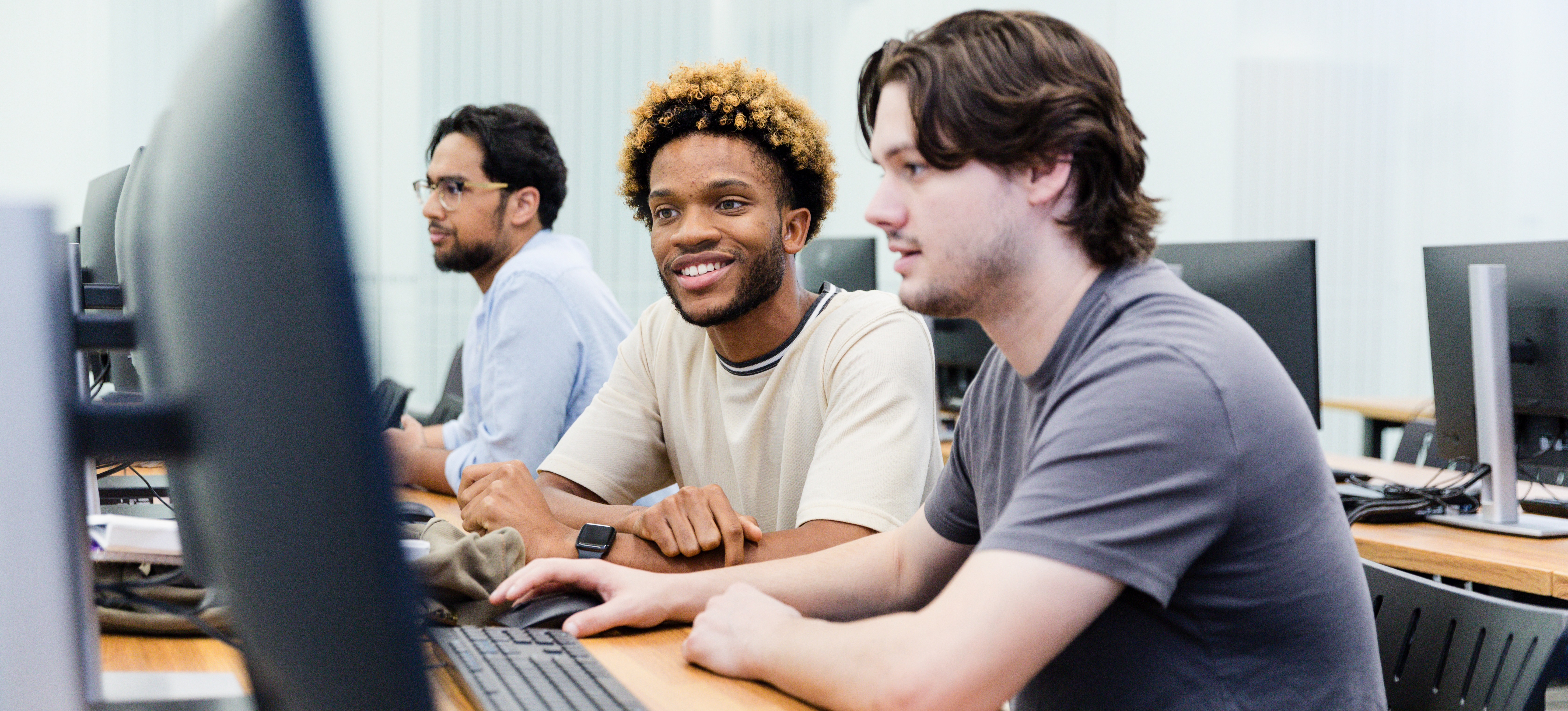 [Featured Image] Three peers sitting at computers, attending a user experience (UX) development boot camp.
