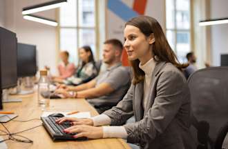 [Featured Image] A woman works in an office and thinks about the pros and cons of her cybersecurity career.