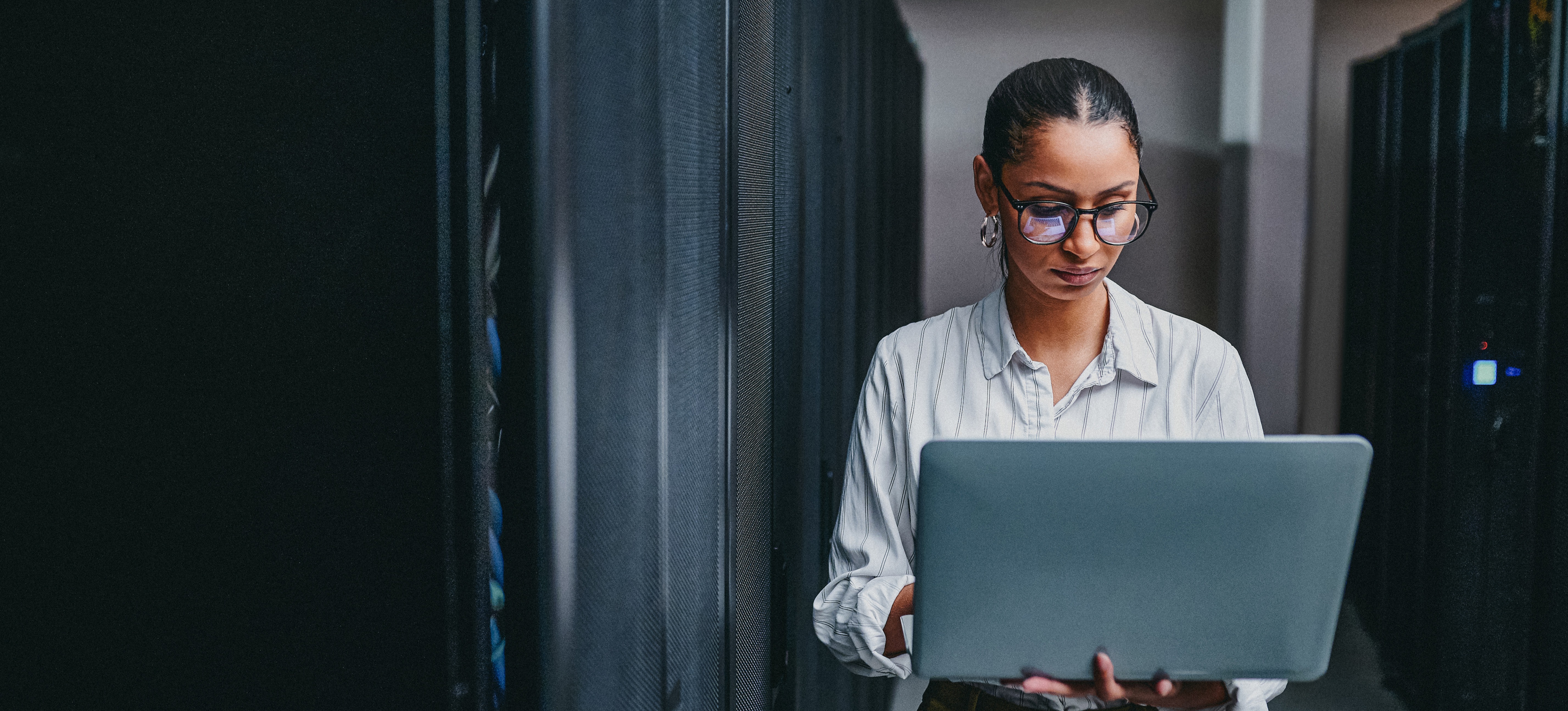 [Featured Image] A person holding a laptop as they stand in the hallway in a database warehouse.
