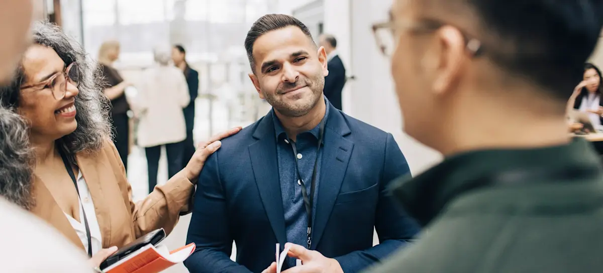 [Featured Image] A professional with good people skills gives eye contact as they listen to a colleague, while another colleague shows validation by putting their hand on their shoulder.