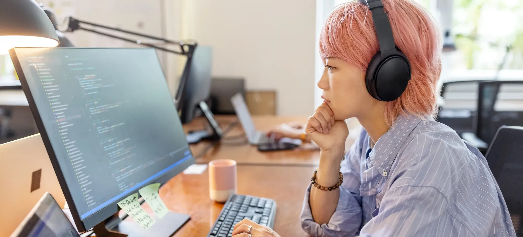 [Featured Image]: A person wearing a blue shirt and wearing headphones reviews code on a computer after exploring how vectors work in C.
